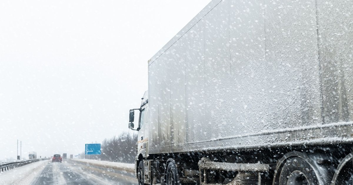 A side view of a white fleet truck driving on the highway through light snow, flurrying backwards.