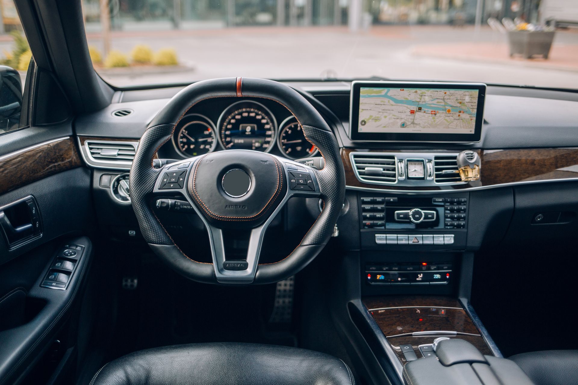 Dashboard of a black Mercedes-Benz, featuring a steering wheel, navigation screen, and wooden accents.