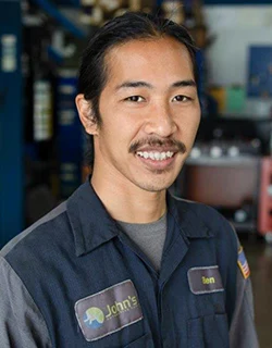 Mechanic in blue uniform smiles in a garage.