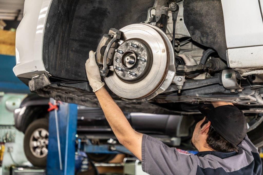 Mechanic working on a car's brakes.  He wears gloves and a cap in a garage.