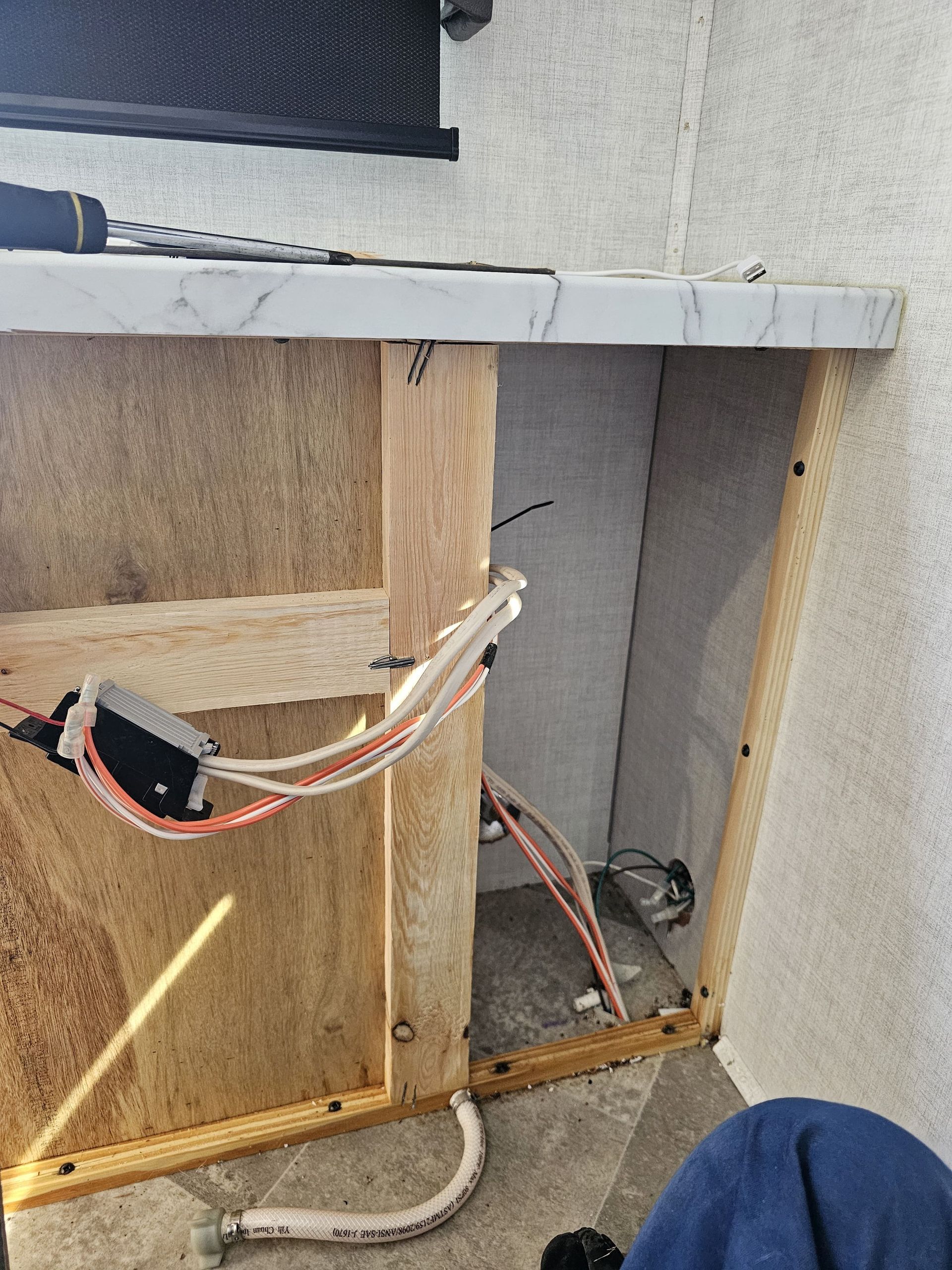 Open cabinet under a counter with exposed wiring, wood framing, and a white pipe in a rough interior wall.