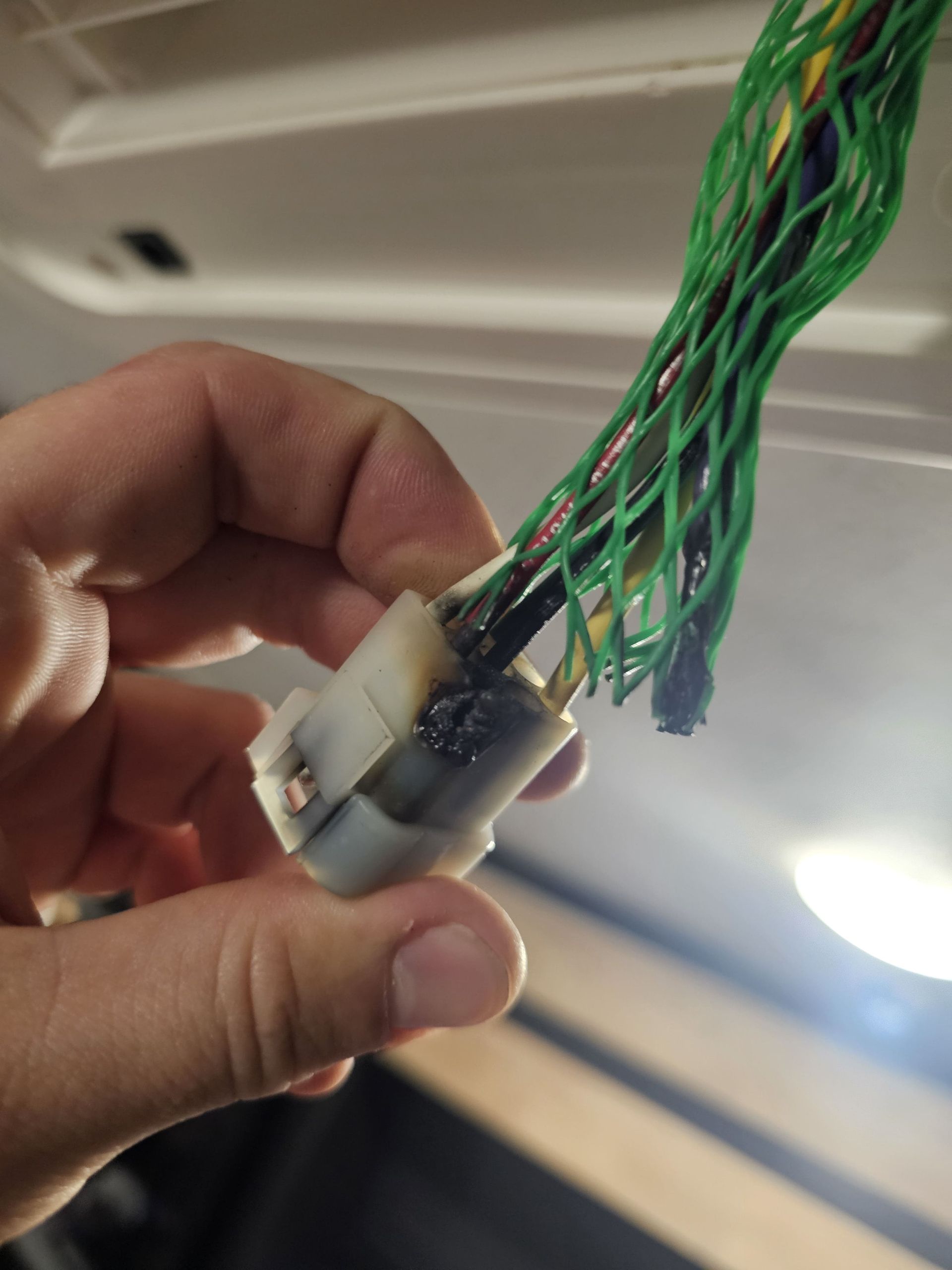 Hand holding a small connector with bundled green wires attached