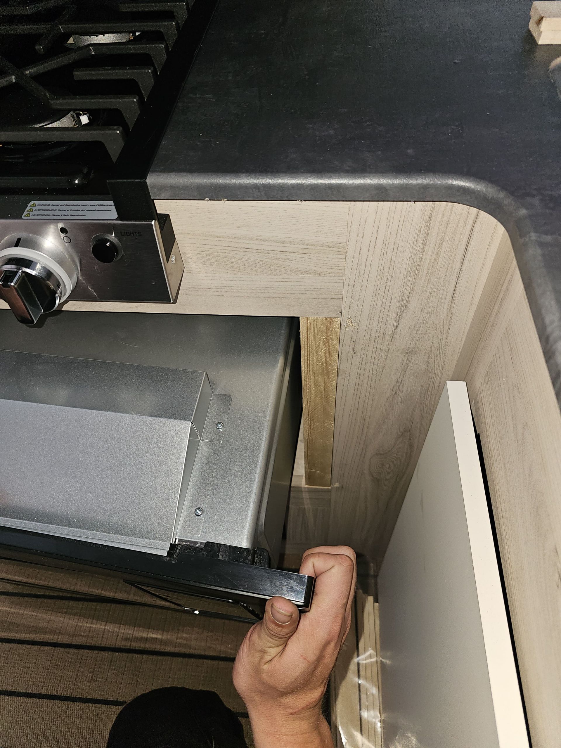 Hand adjusting a black metal drawer or tray inside a cabinet beside a wood panel.