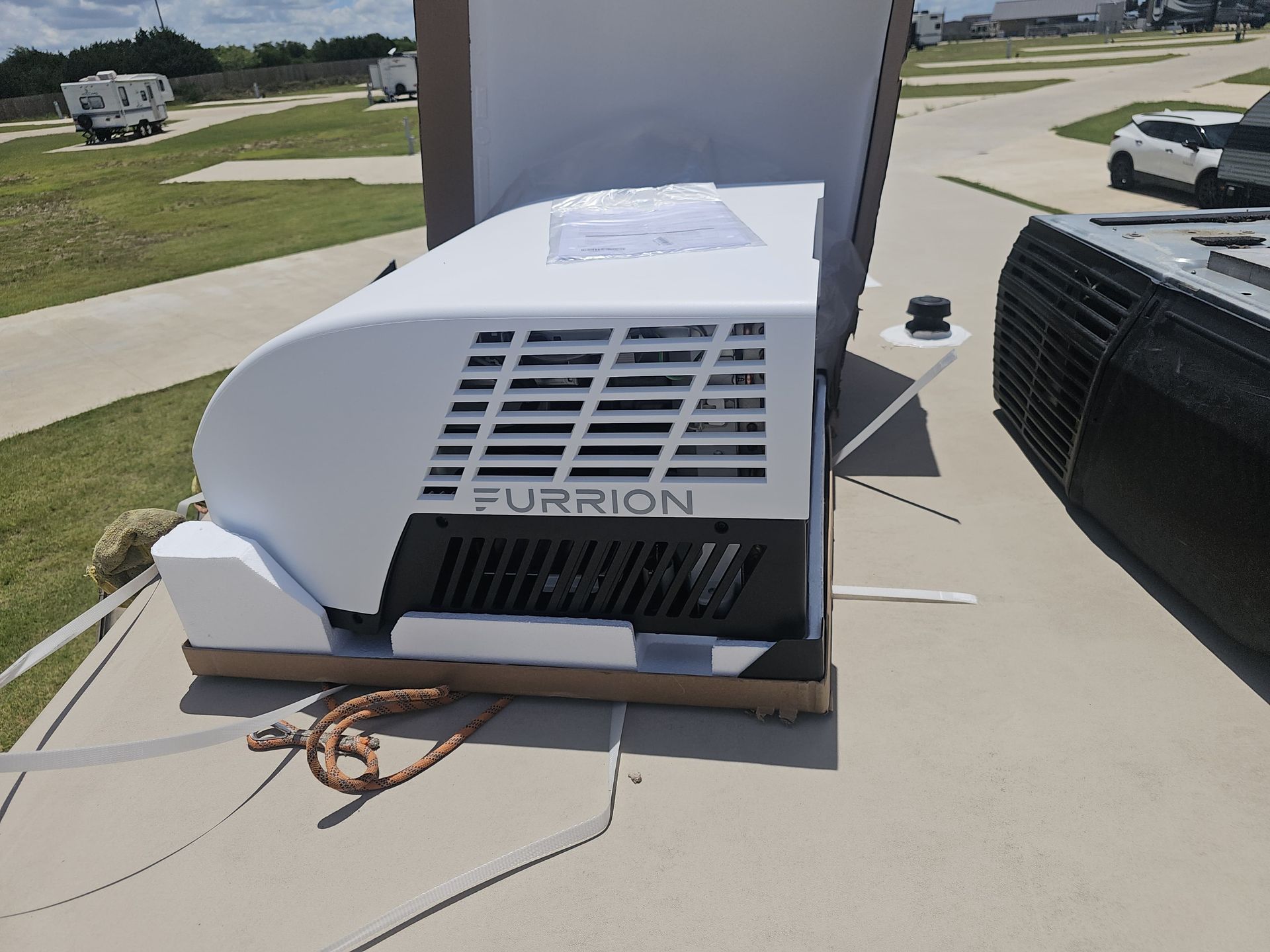 White Furrion RV rooftop air conditioner with exposed wires on an RV roof, near a suburban street