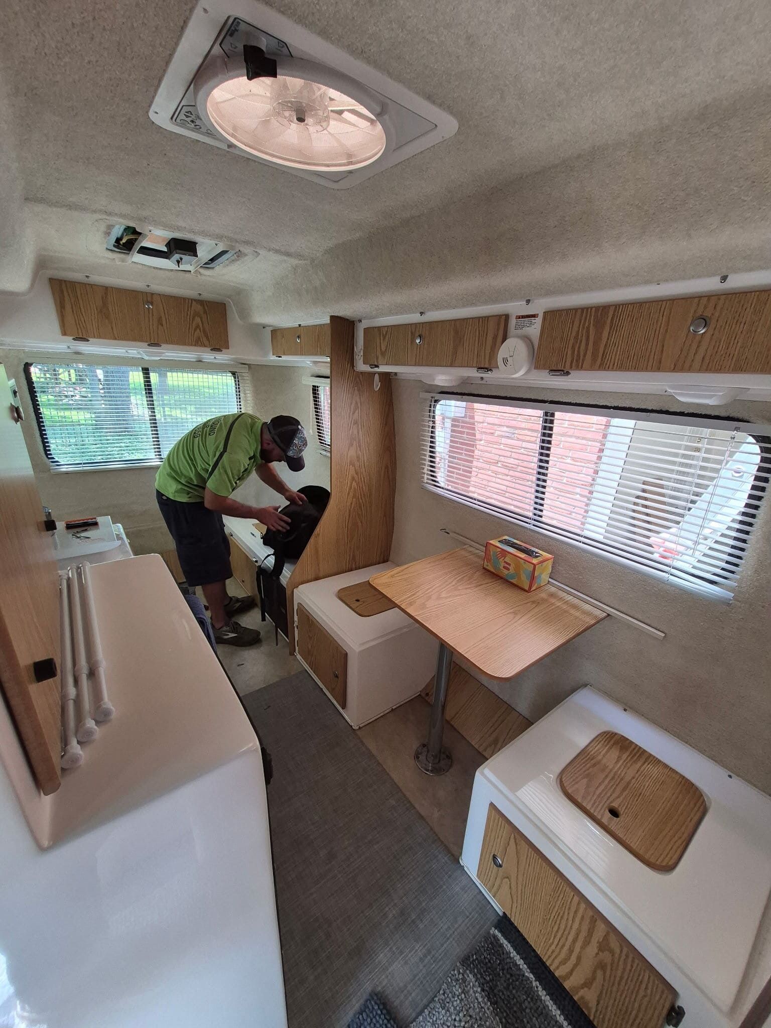 Person packing inside a small camper van with a white table, bench seat, and windows with blinds.