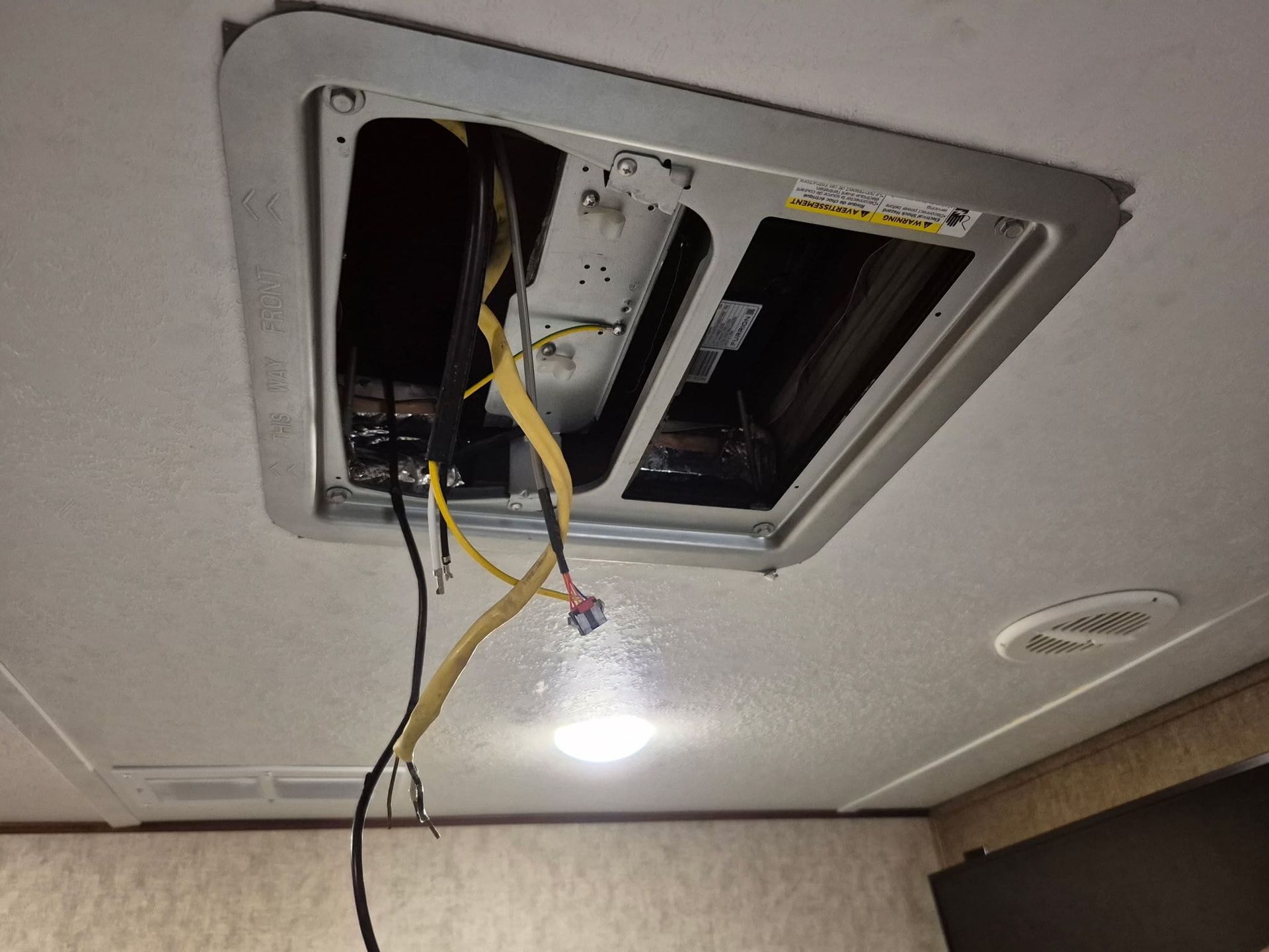 Open ceiling with exposed wires and a recessed light fixture being repaired