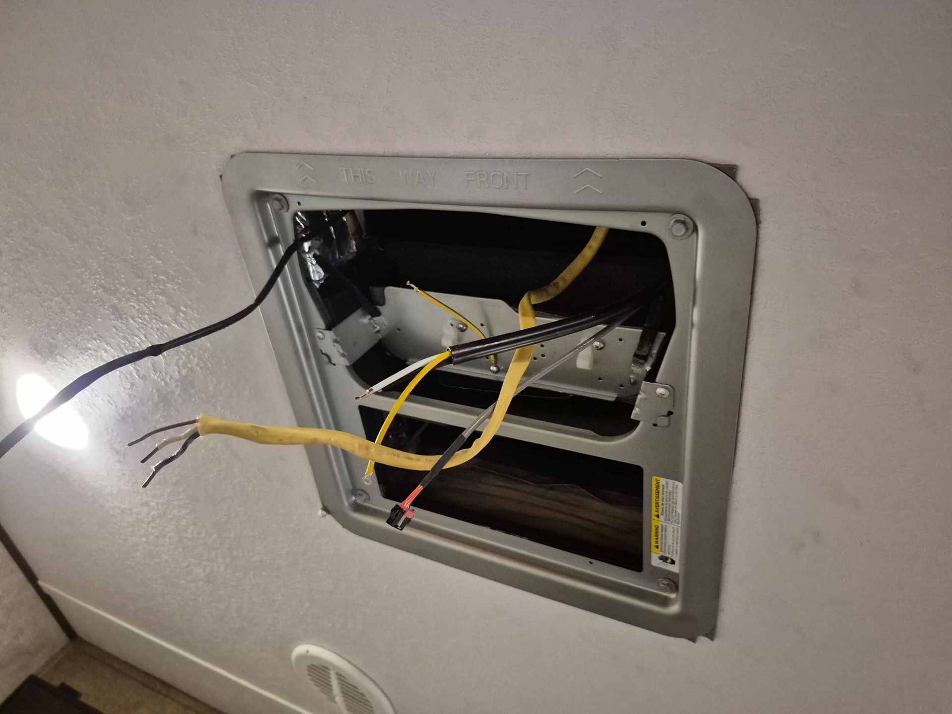 Wall-mounted HVAC unit with an open panel and exposed yellow and black wires hanging out