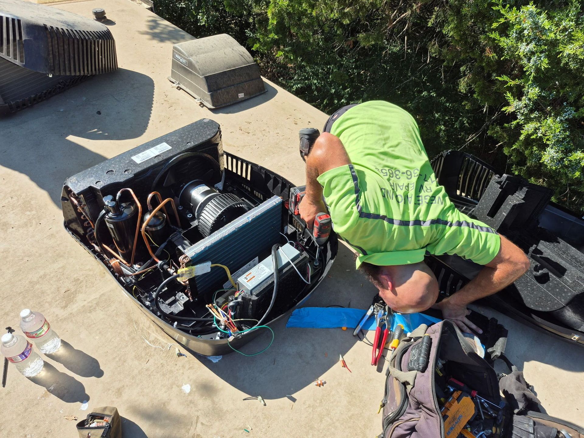 Technician in neon green shirt working on exposed rooftop HVAC unit with tools nearby