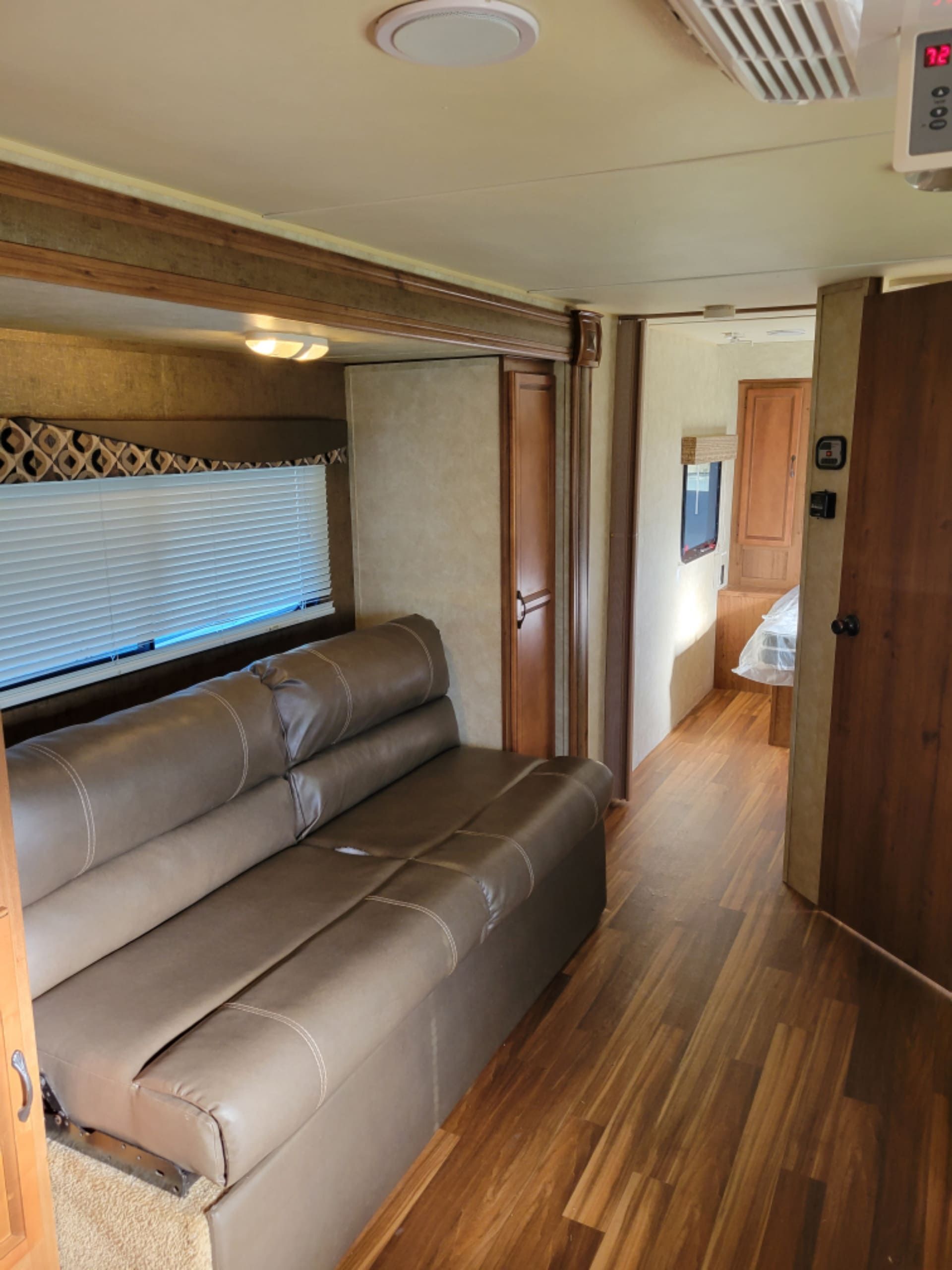 Interior of a compact RV with a tan leather sofa, wood flooring, and a narrow hallway leading to the back room