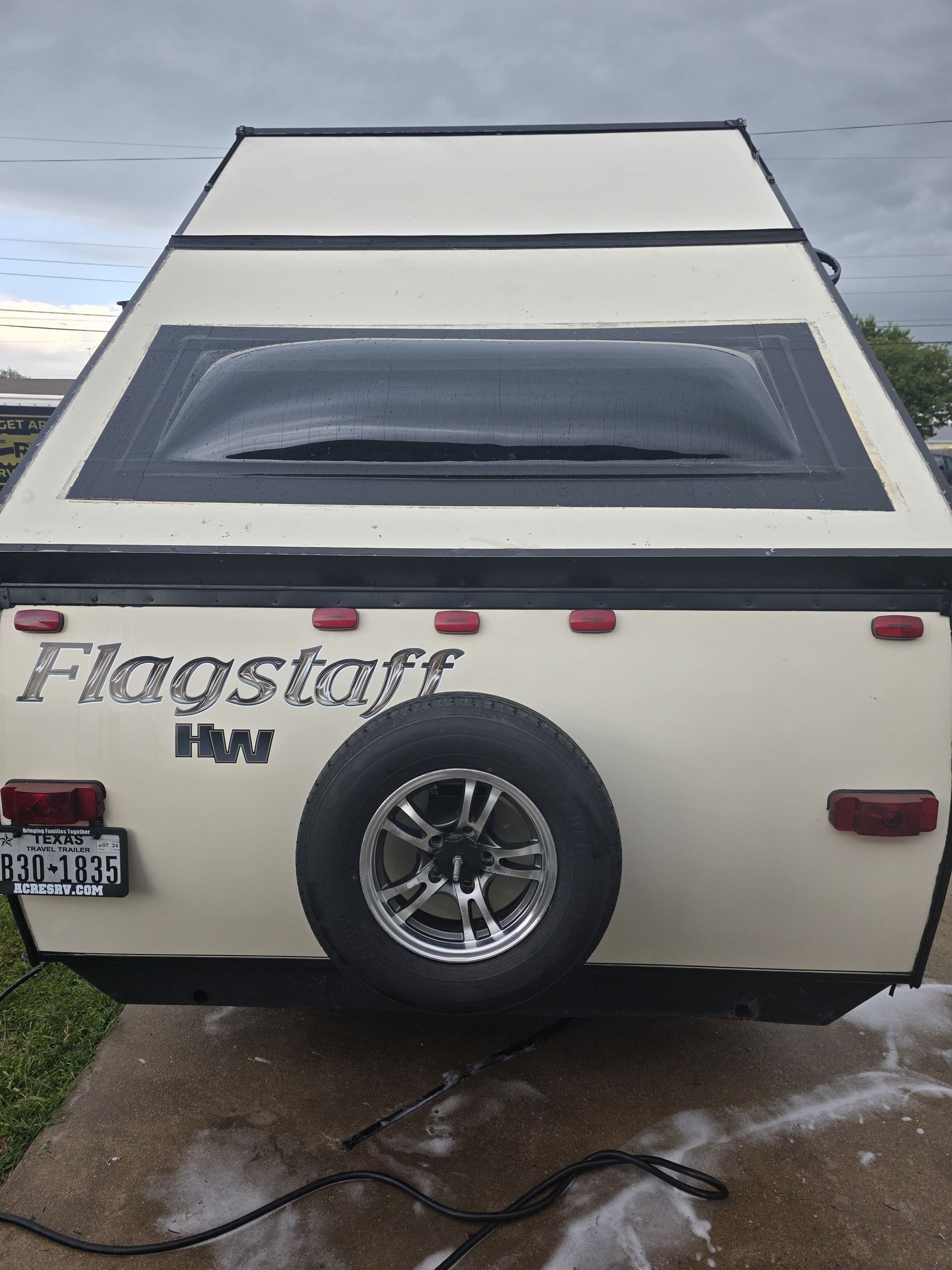 Rear view of a cream-colored Flagstaff H/W camper with spare tire, parked on wet pavement.