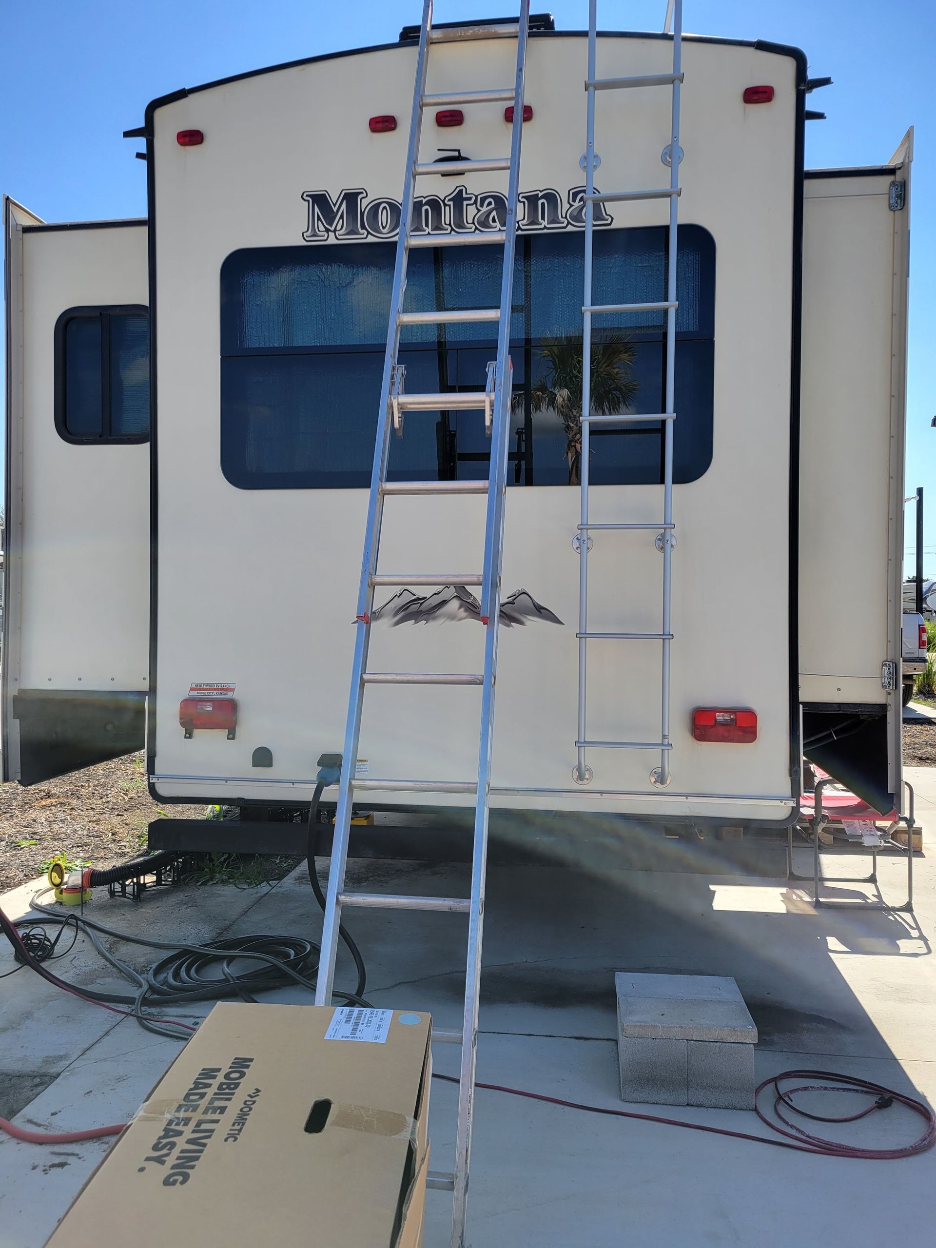 Back of a white RV with a ladder, parked outdoors on a sunny lot