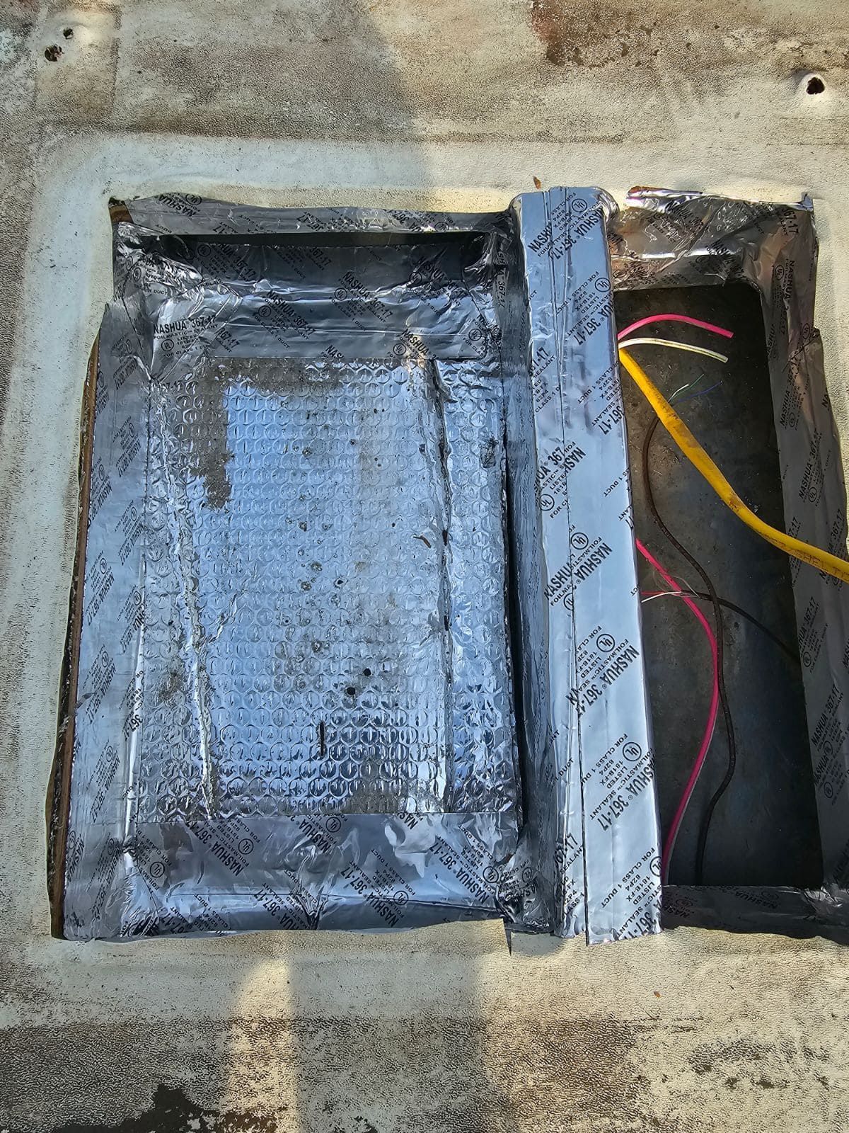 Open electrical box with wiring and a black lid on a concrete surface.