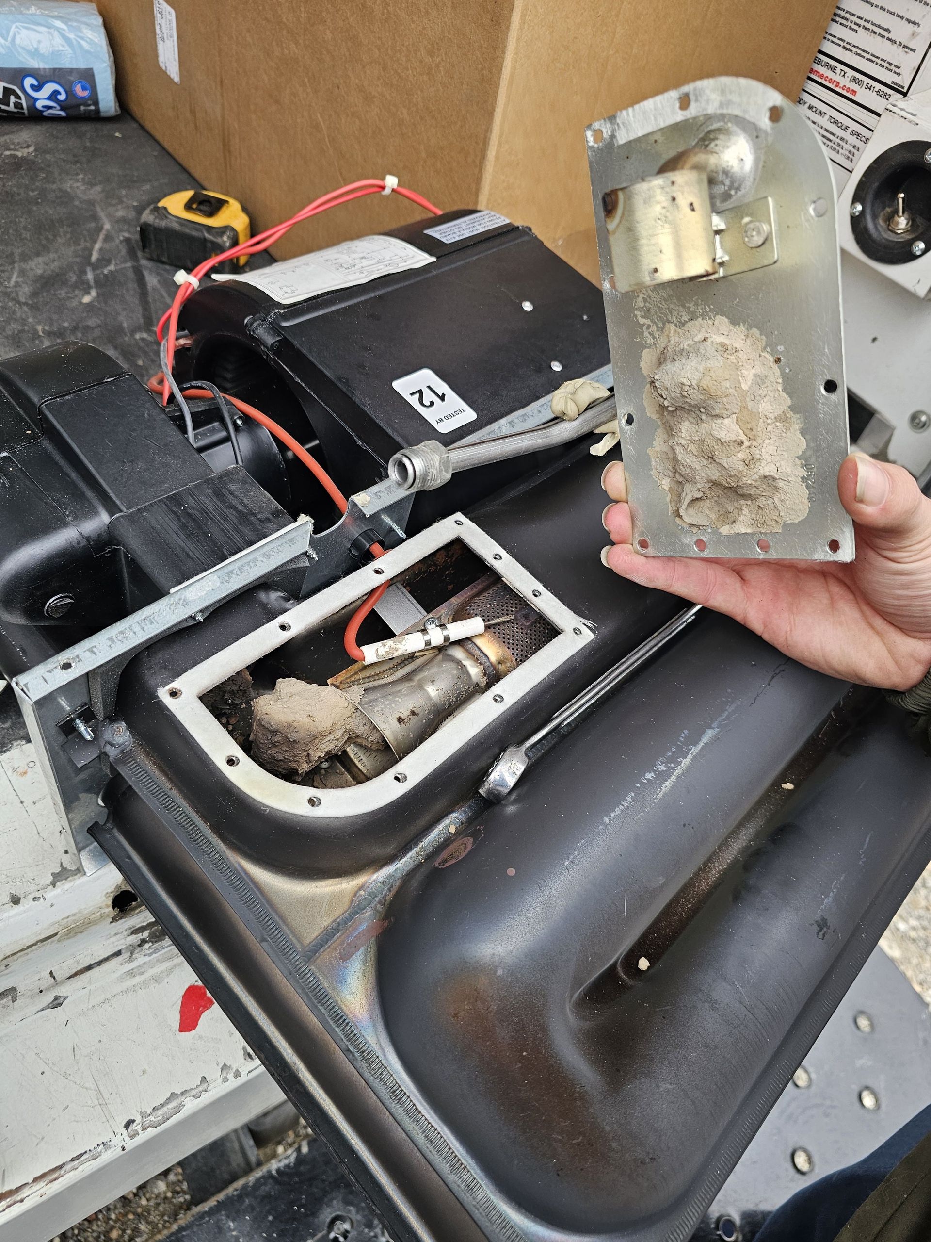 Damaged battery compartment with corroded wiring and a removed rusted metal panel held in hand