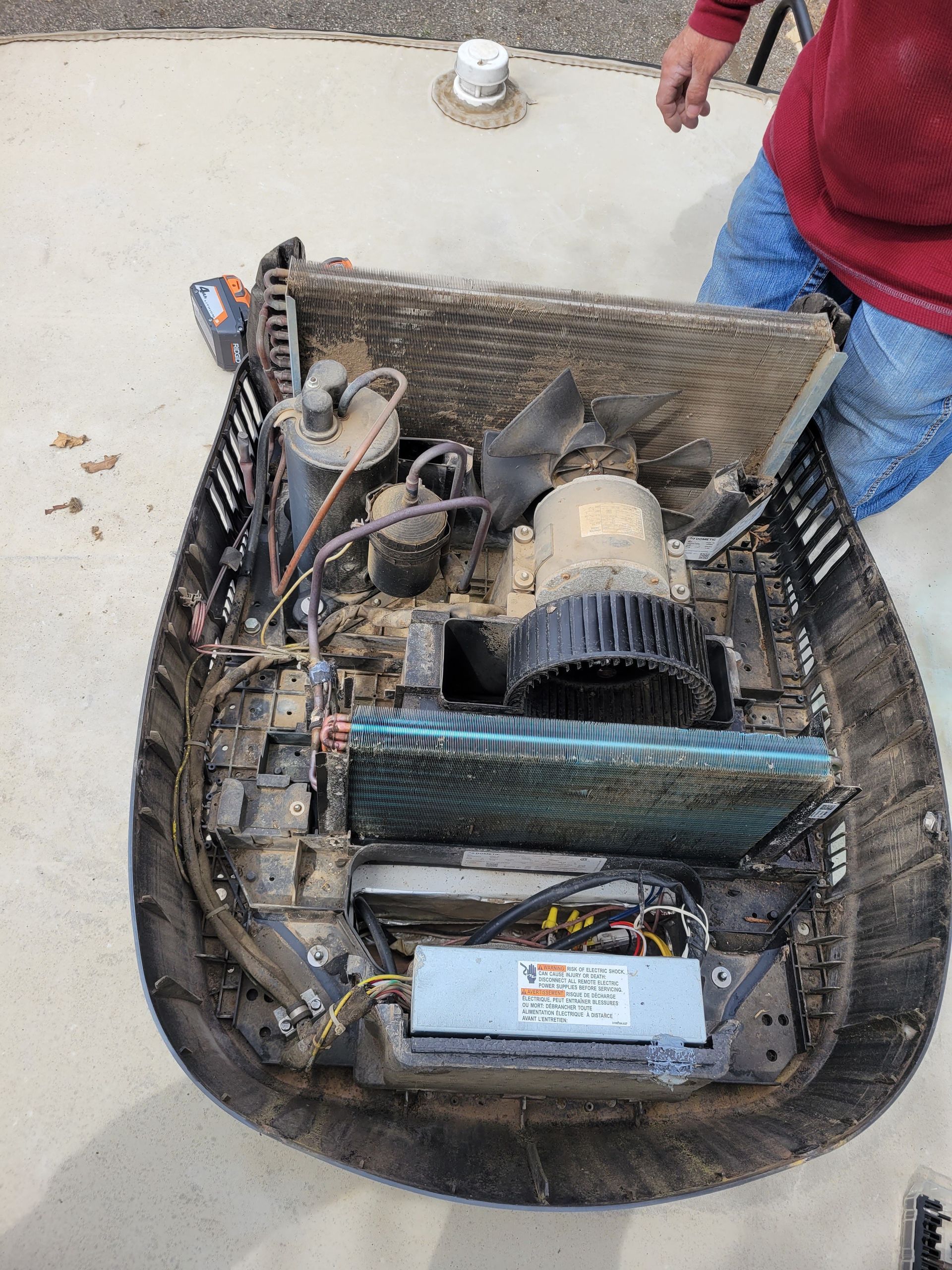 Open hoverboard with exposed motor, battery, and wiring on concrete, with a person nearby
