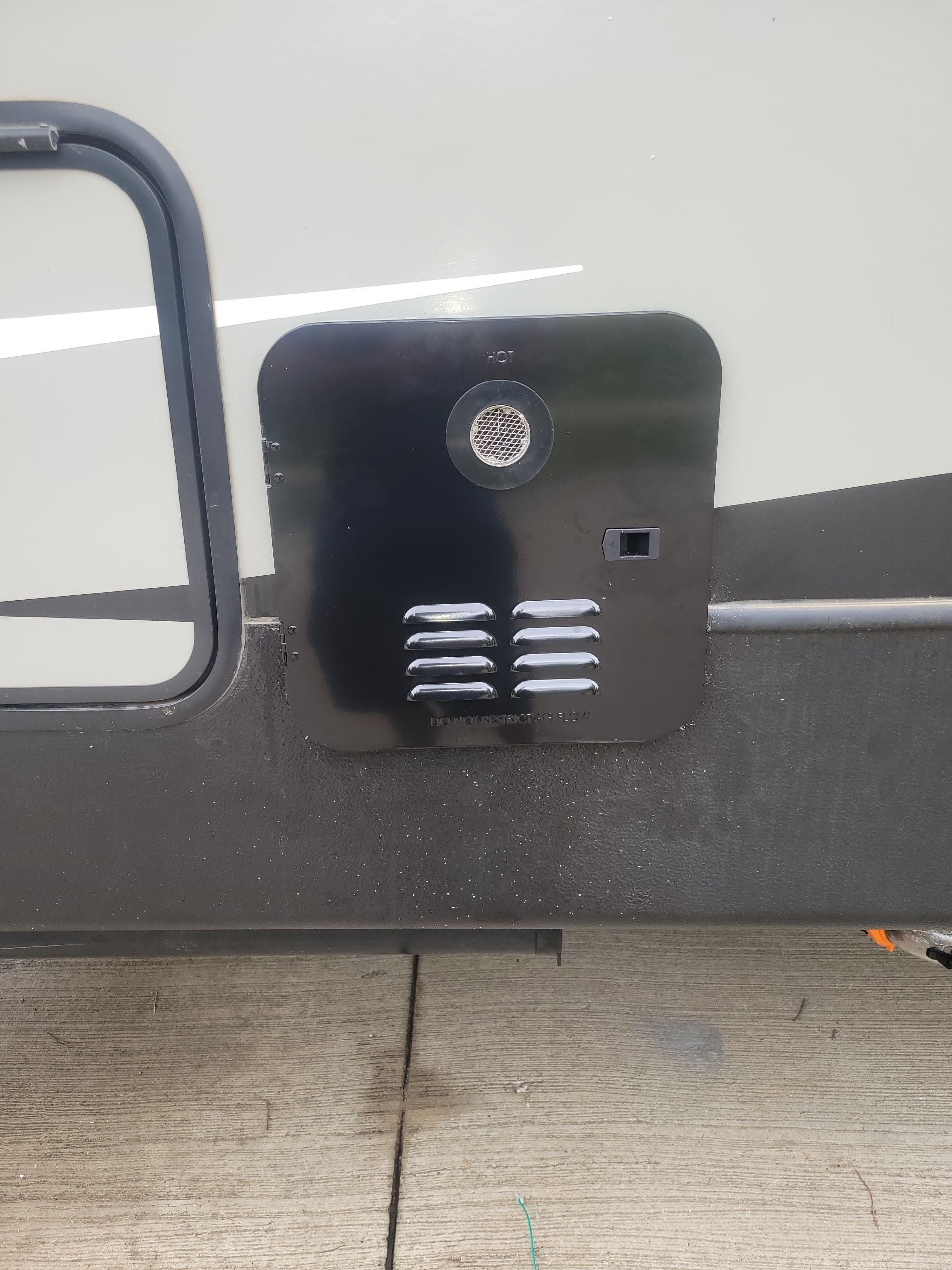 Black wall-mounted vent with a small gauge on a vehicle or trailer side panel.
