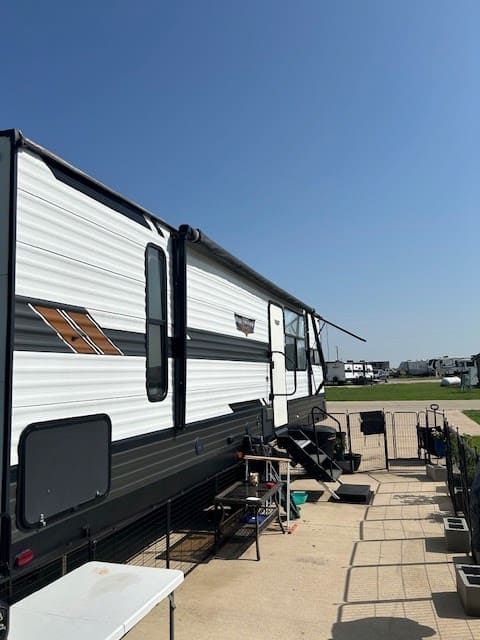 White-and-black RV with extended awning parked on a paved lot under a clear blue sky.