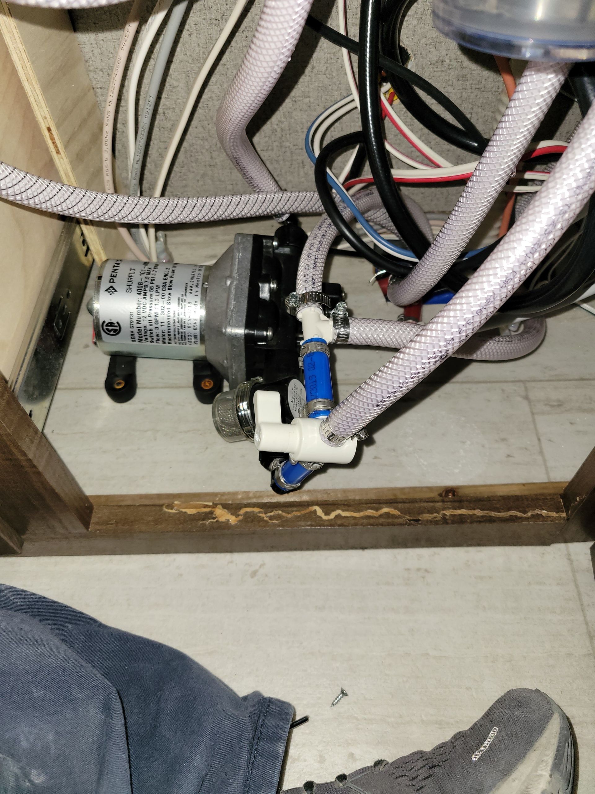 Close-up of under-sink plumbing with hoses, wires, and a small motor assembly in a cabinet.