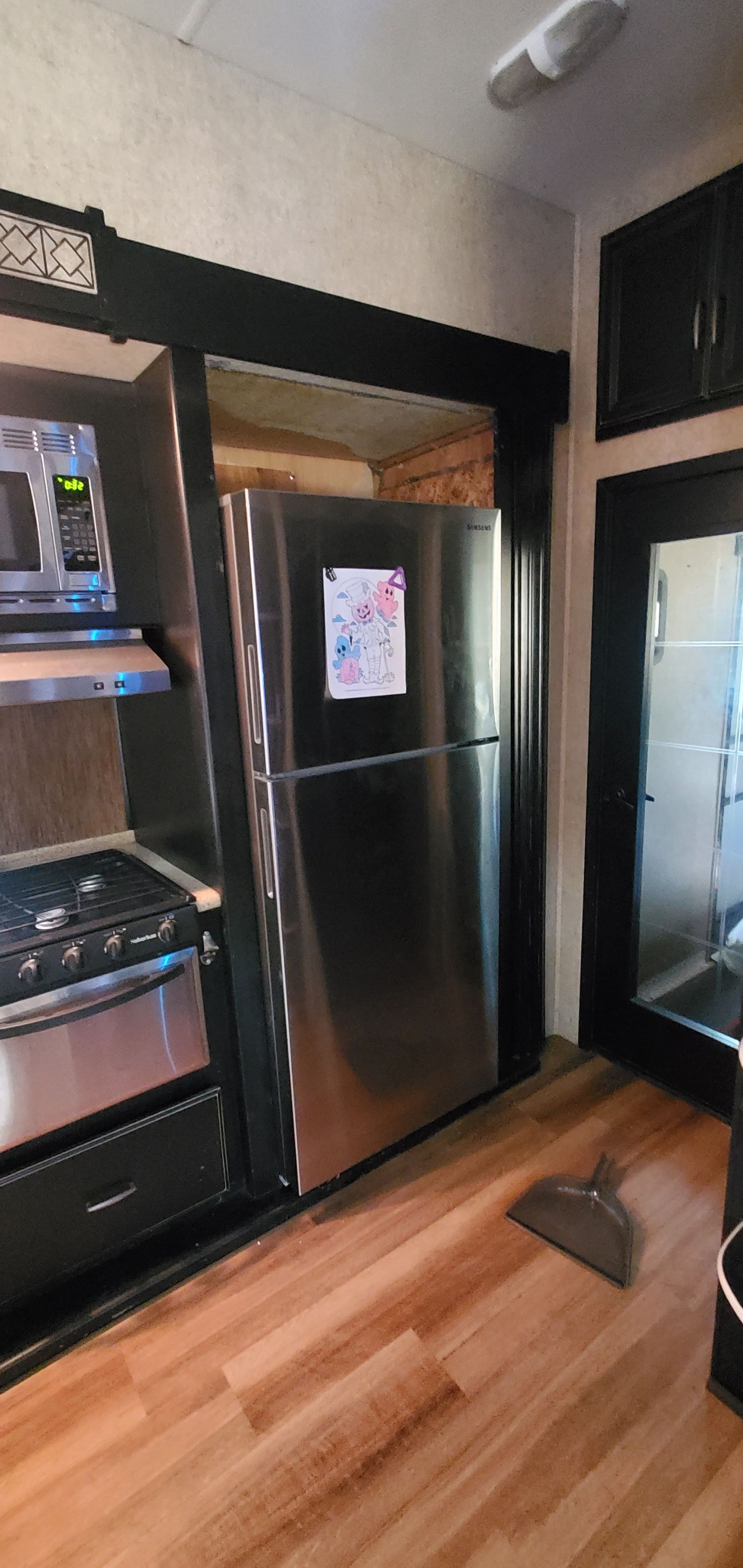 Kitchen with black refrigerator, stainless steel oven, and built-in microwave against dark cabinetry