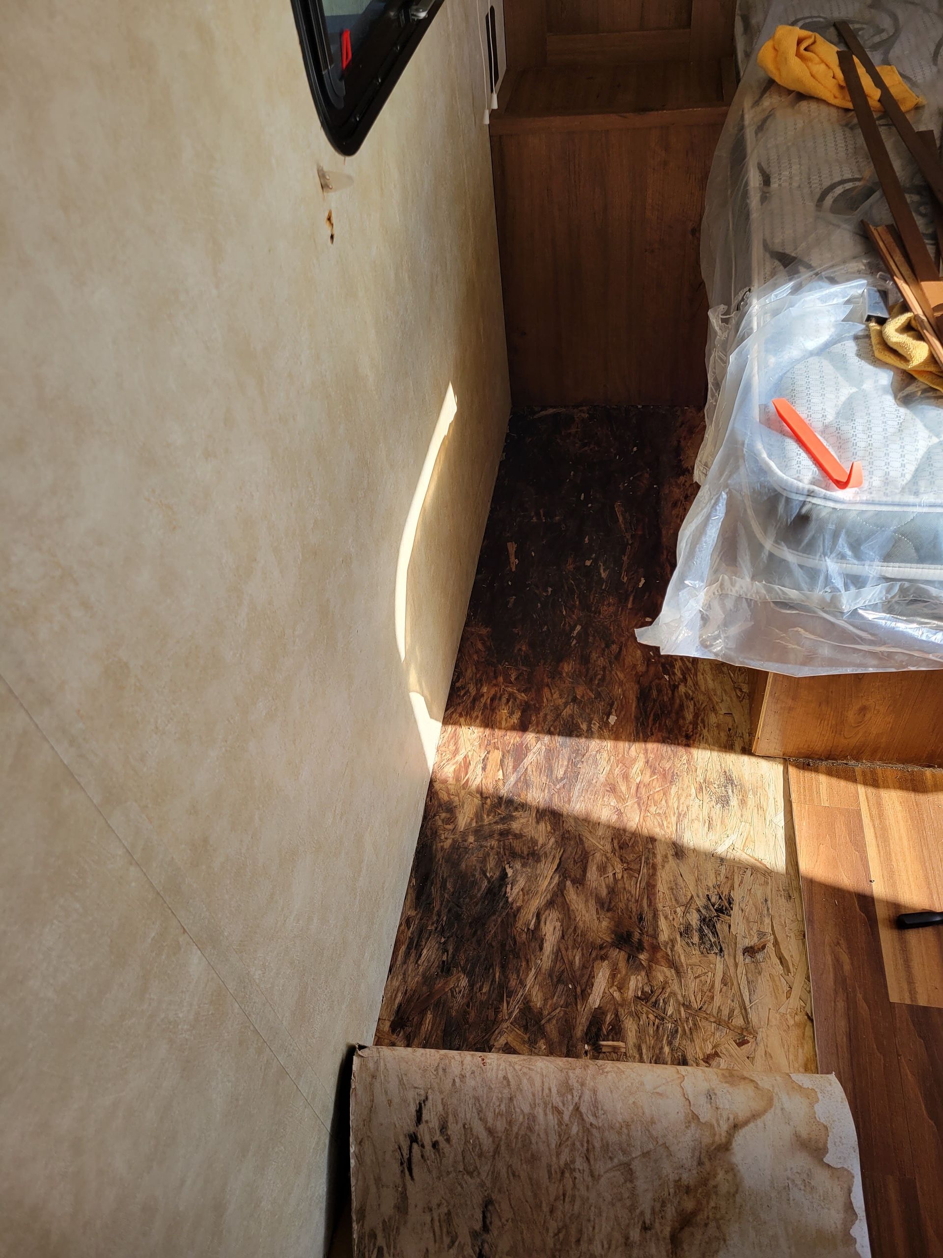 Sunlit corner of a room with a stained floor, wall, and a plastic-covered object in the right corner