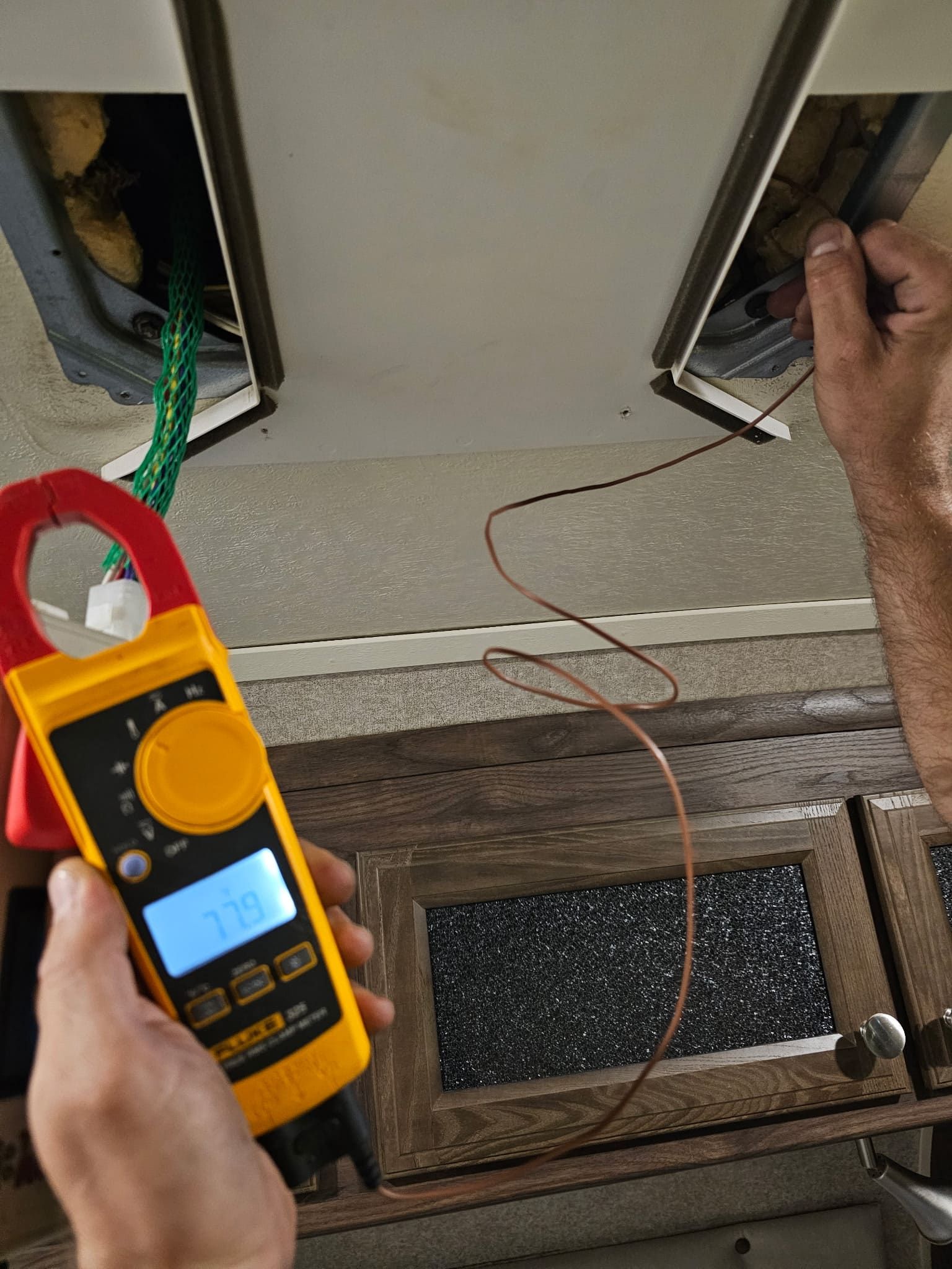 Hands using a yellow multimeter to test wiring in an open electrical panel.