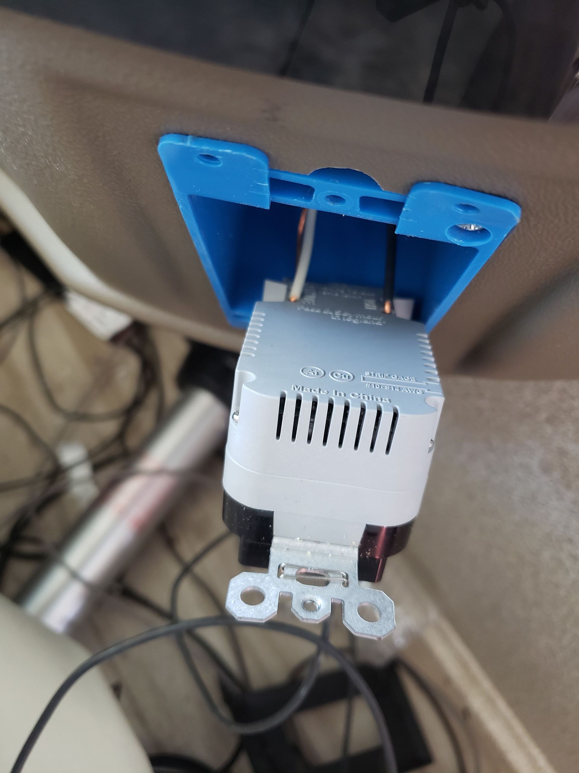 White outlet tester with blue clip mounted on a beige wall, with cables visible below