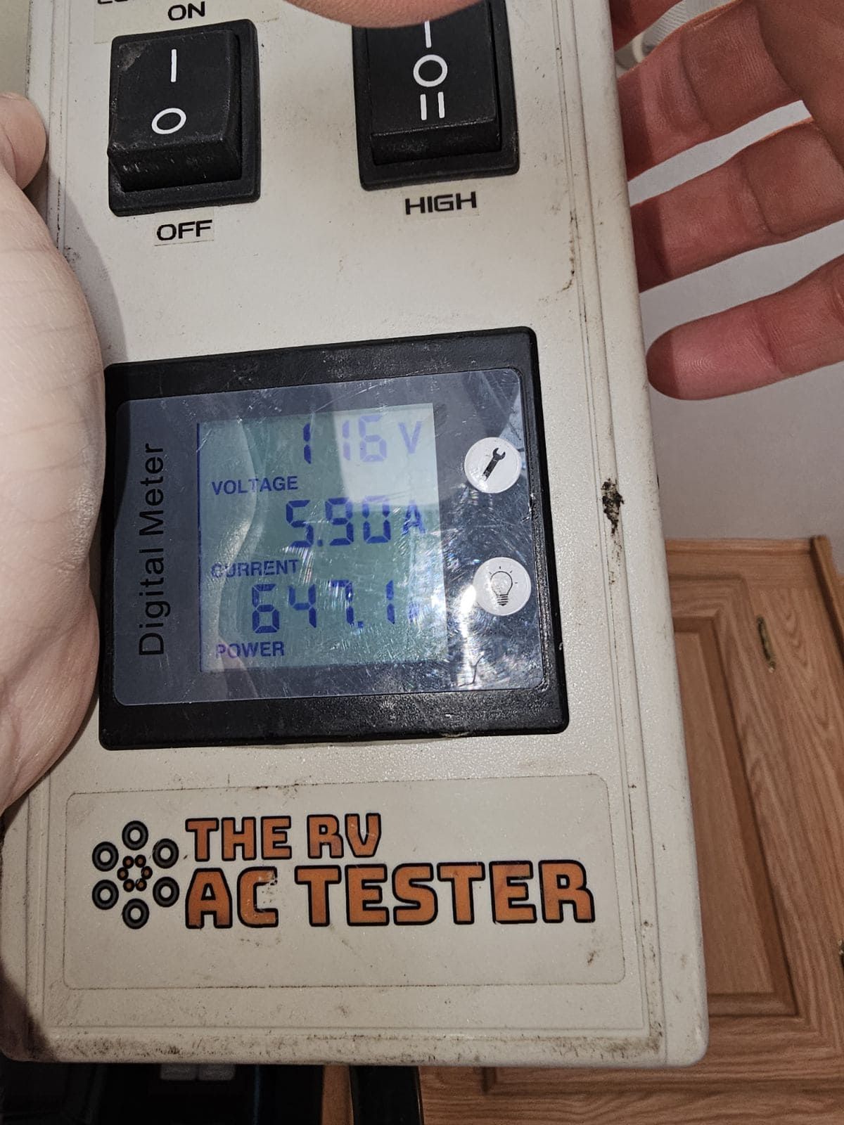 Handheld RV AC tester with illuminated digital display and two black toggle switches above it