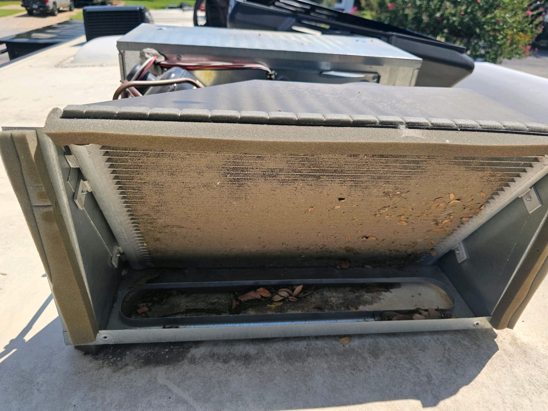 Open metal HVAC unit with a dirty, clogged filter and leaves inside, on a rooftop.