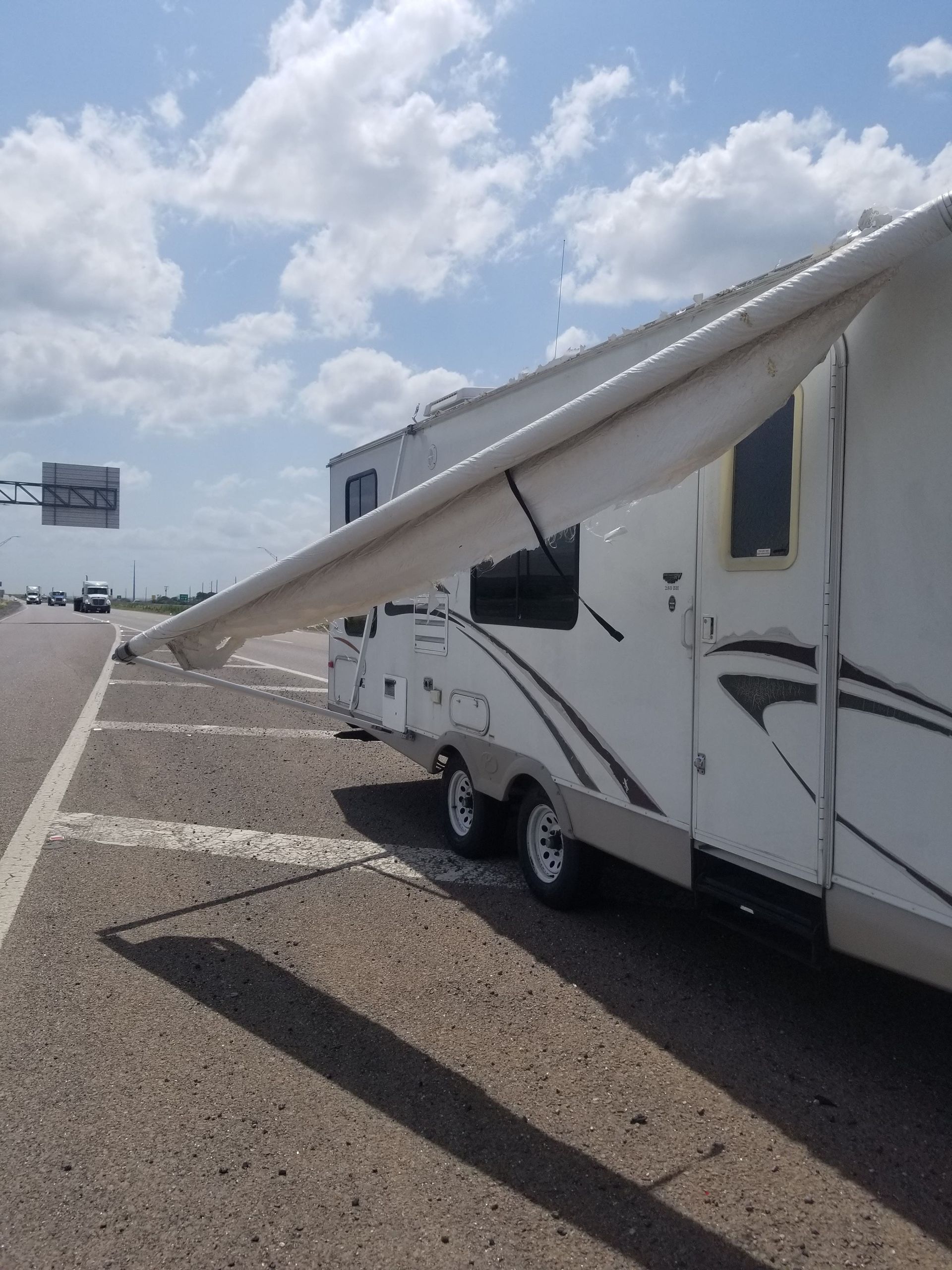 White RV with extended awning parked on a roadside under a partly cloudy sky