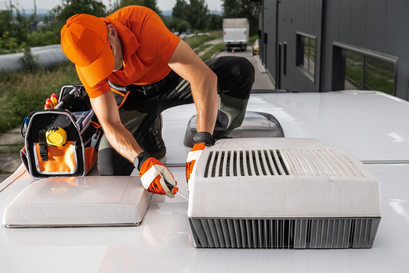 Worker in orange shirt repairing rooftop HVAC units beside a lit portable work light.