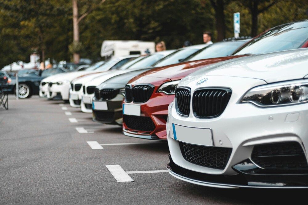 A row of modern luxury sports cars parked in a neat line outdoors, focusing closely on the distinctive front grille of a white car.