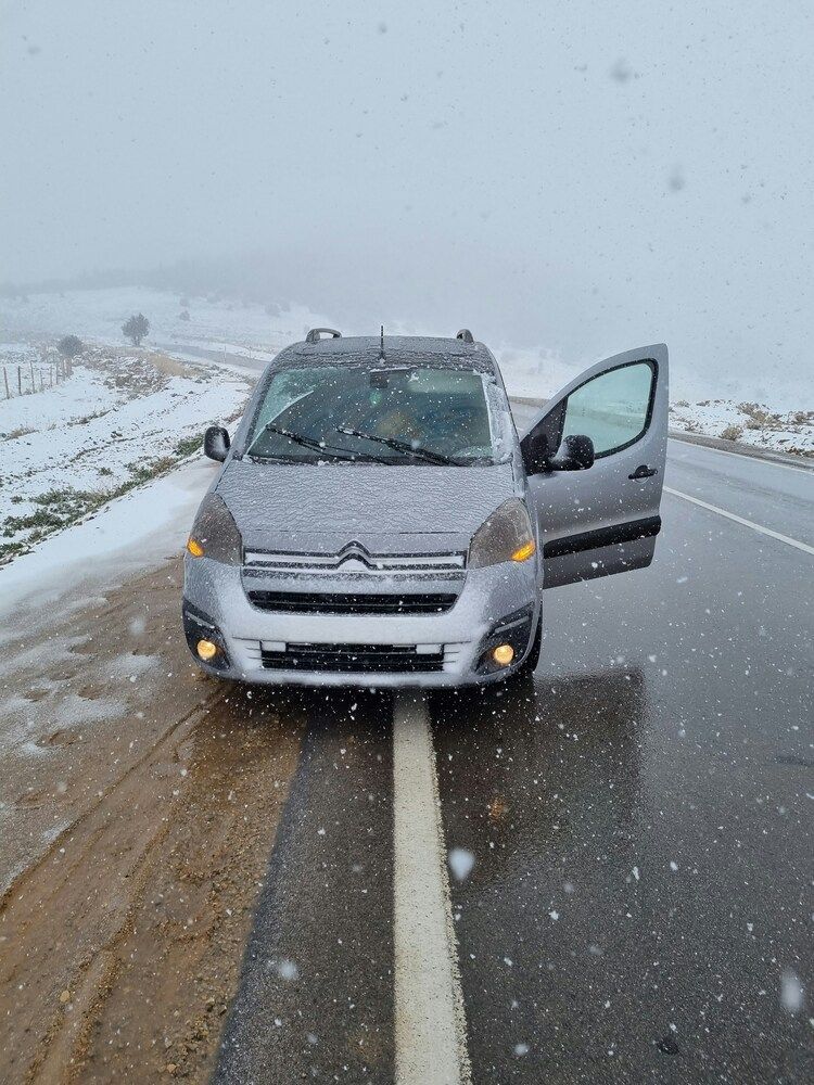 A front-view shot of a silver Citroën compact van pulled over on a wet asphalt road during an active winter snowstorm.