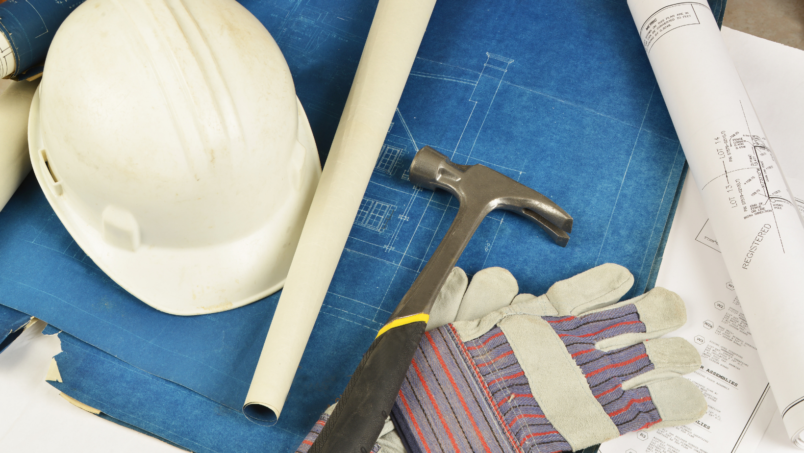 A hard hat a hammer and gloves are on top of a blueprint