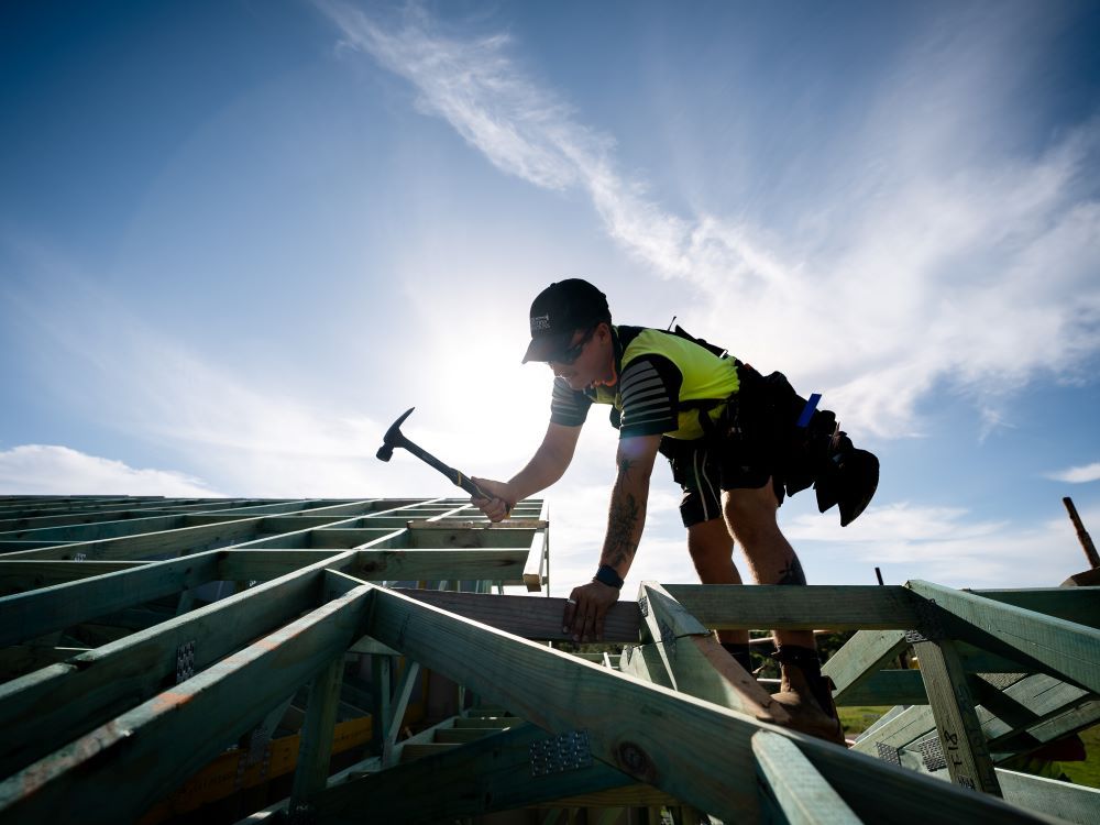 A Man Is Working On The Roof Of A Building With A Hammer — J.White Carpentry & Renovations in Port Macquarie, NSW