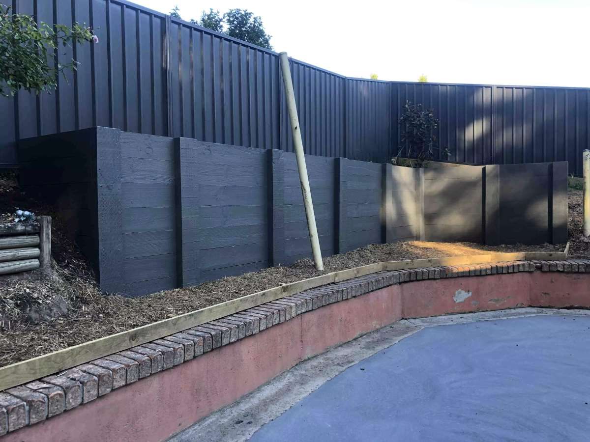 A black fence is surrounding a brick wall in a backyard. — J.White Carpentry & Renovations in Port Macquarie, NSW 