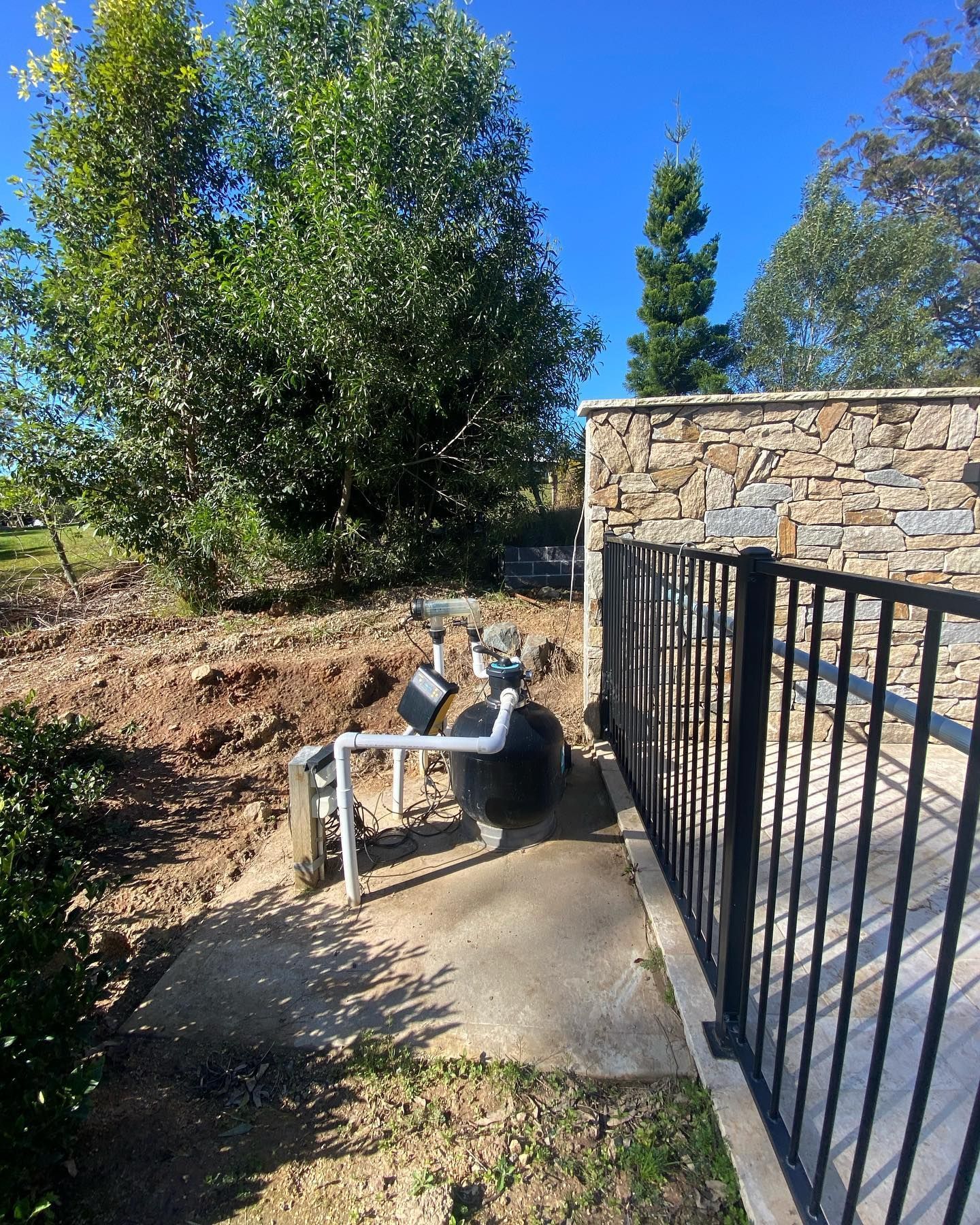 A black fence surrounds a concrete walkway next to a stone wall. — J.White Carpentry & Renovations in Port Macquarie, NSW 