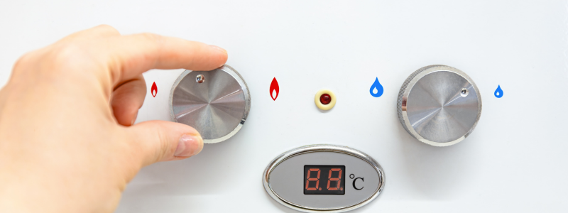 Hand adjusting a silver shower temperature knob with hot and cold icons on a white wall control panel