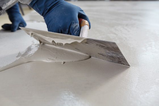Gloved hand spreading gray plaster with a trowel on a smooth surface