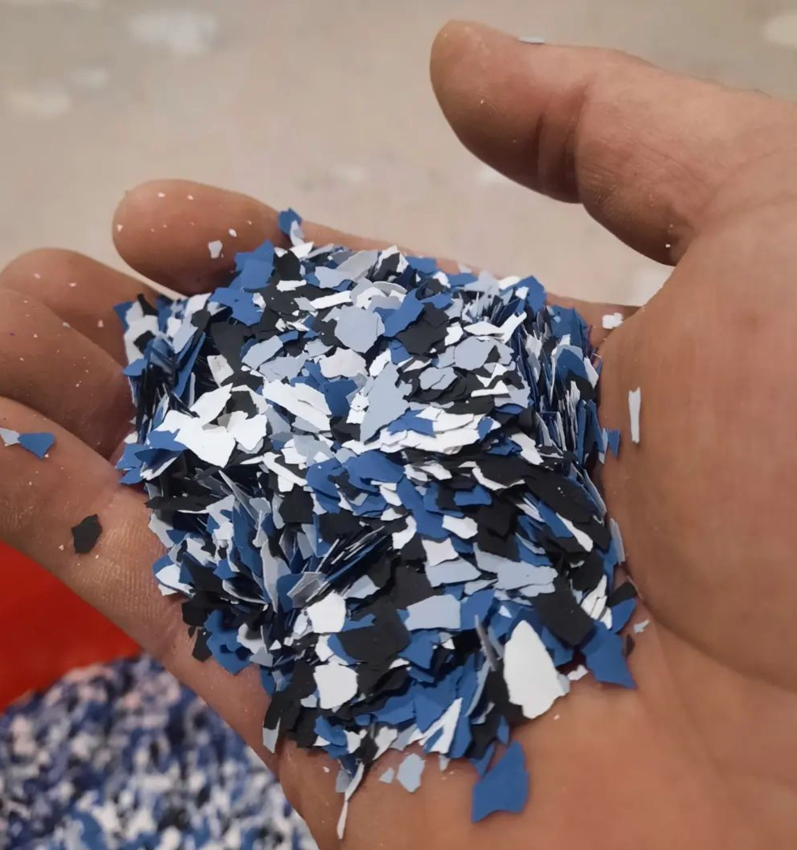 Hand holding a pile of blue, white, and black plastic confetti or flakes