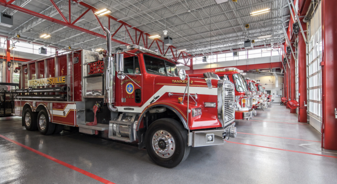 Red fire truck parked inside a modern fire station bay with red accents and bright overhead lights