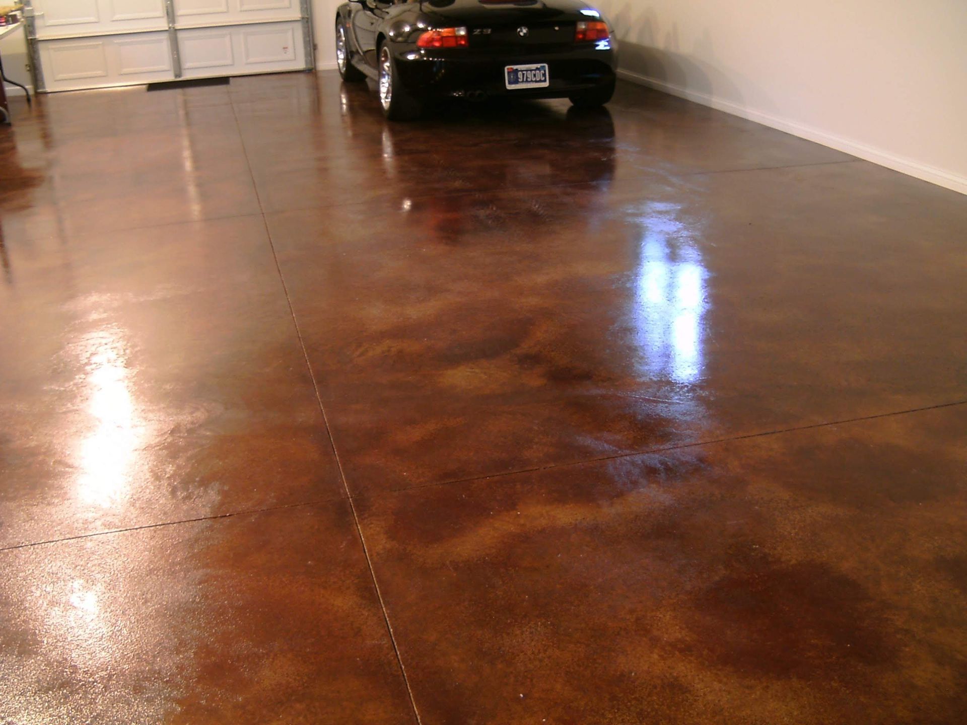 Shiny brown garage floor with a black car parked near the back wall.