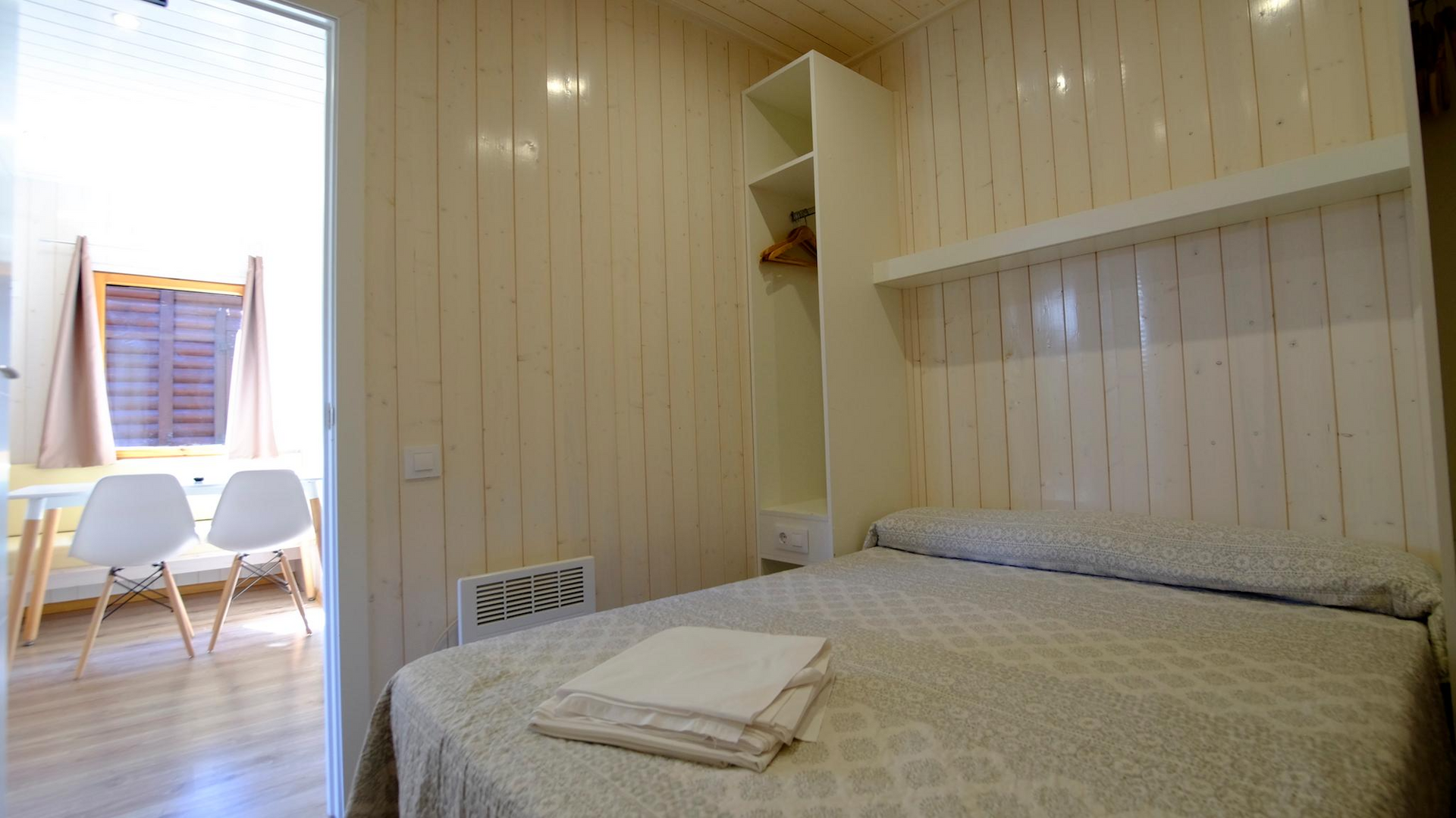 Dormitorio con cama, pequeño armario y puerta abierta a una zona de estar.