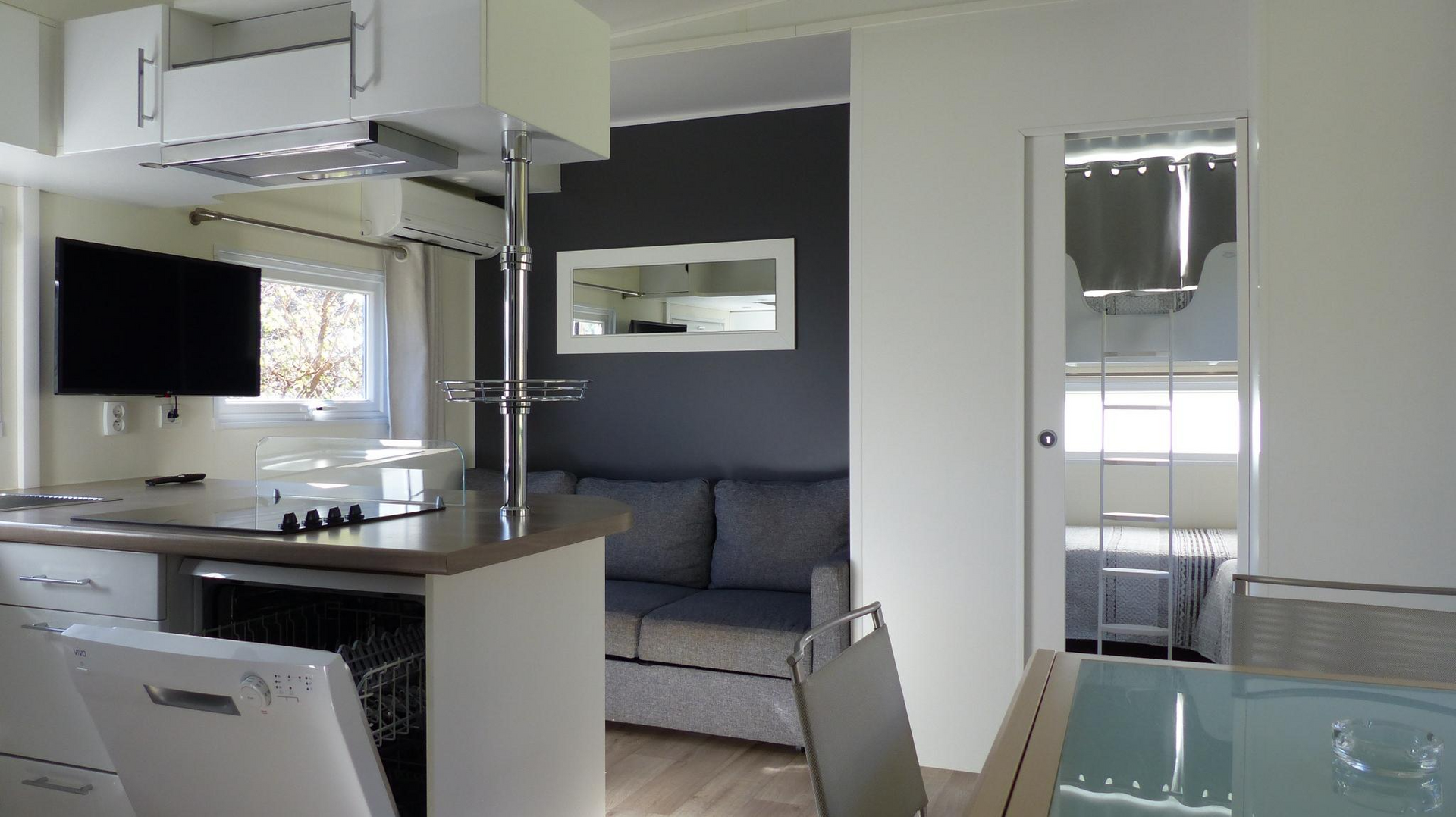 Interior moderno con cocina, sala de estar y dormitorio a la vista. Acabados en gris, blanco y acero inoxidable.