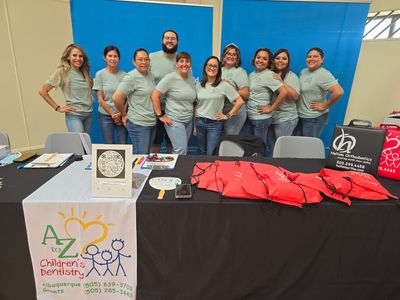 AZ Children's Dentistry team stands behind a table with brochures and giveaways. AZ Children's Dentistry team stands behind a table with brochures and giveaways.