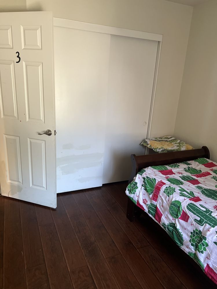 Small bedroom with white walls, dark wood floor, and a bed with a colorful quilt.