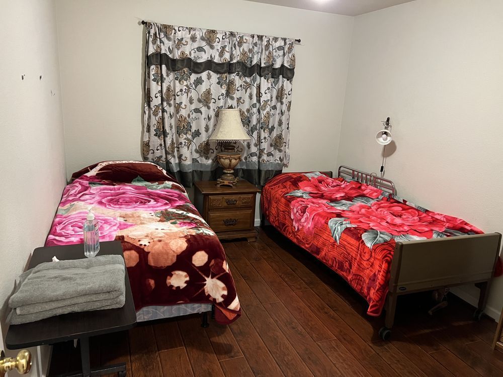 Bedroom with two single beds, floral red bedding, a nightstand, lamp, and patterned curtains