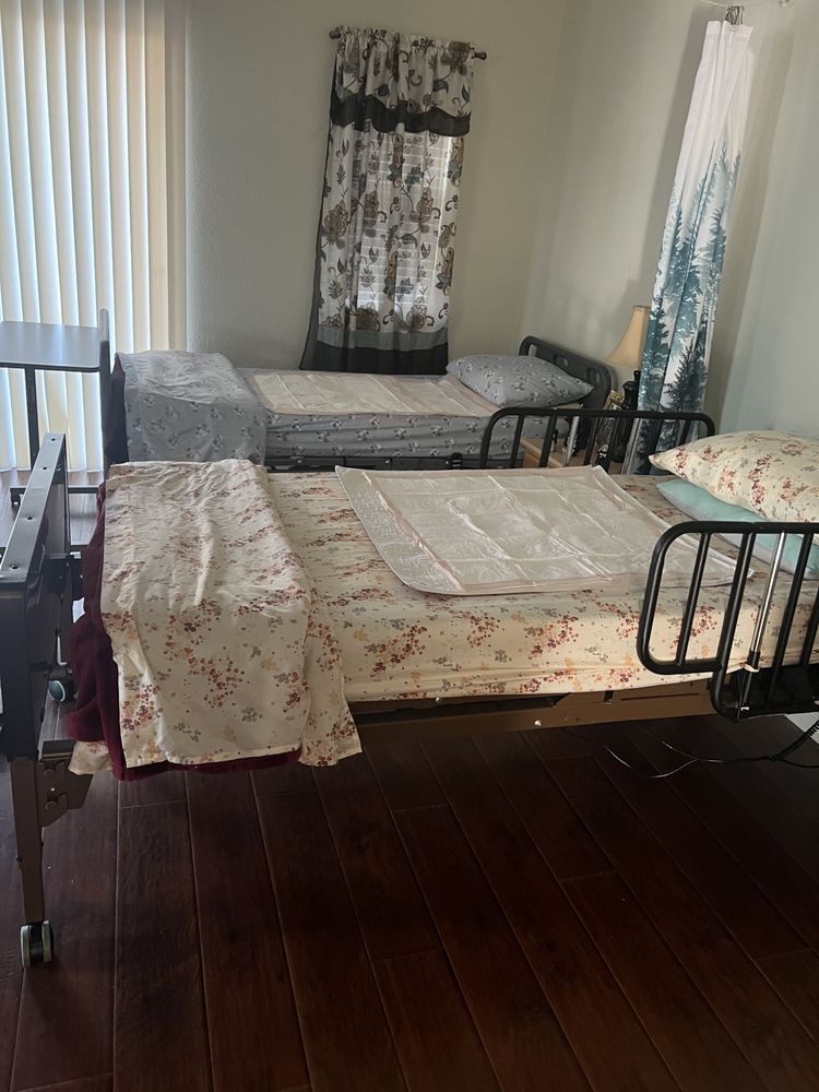 Room with two twin beds, dark wood floor, floral bedding, and large windows with sheer curtains.