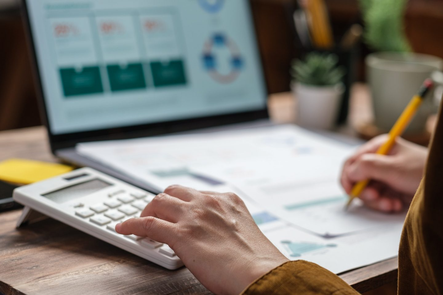Person using a calculator while reviewing financial documents and a laptop displaying charts.