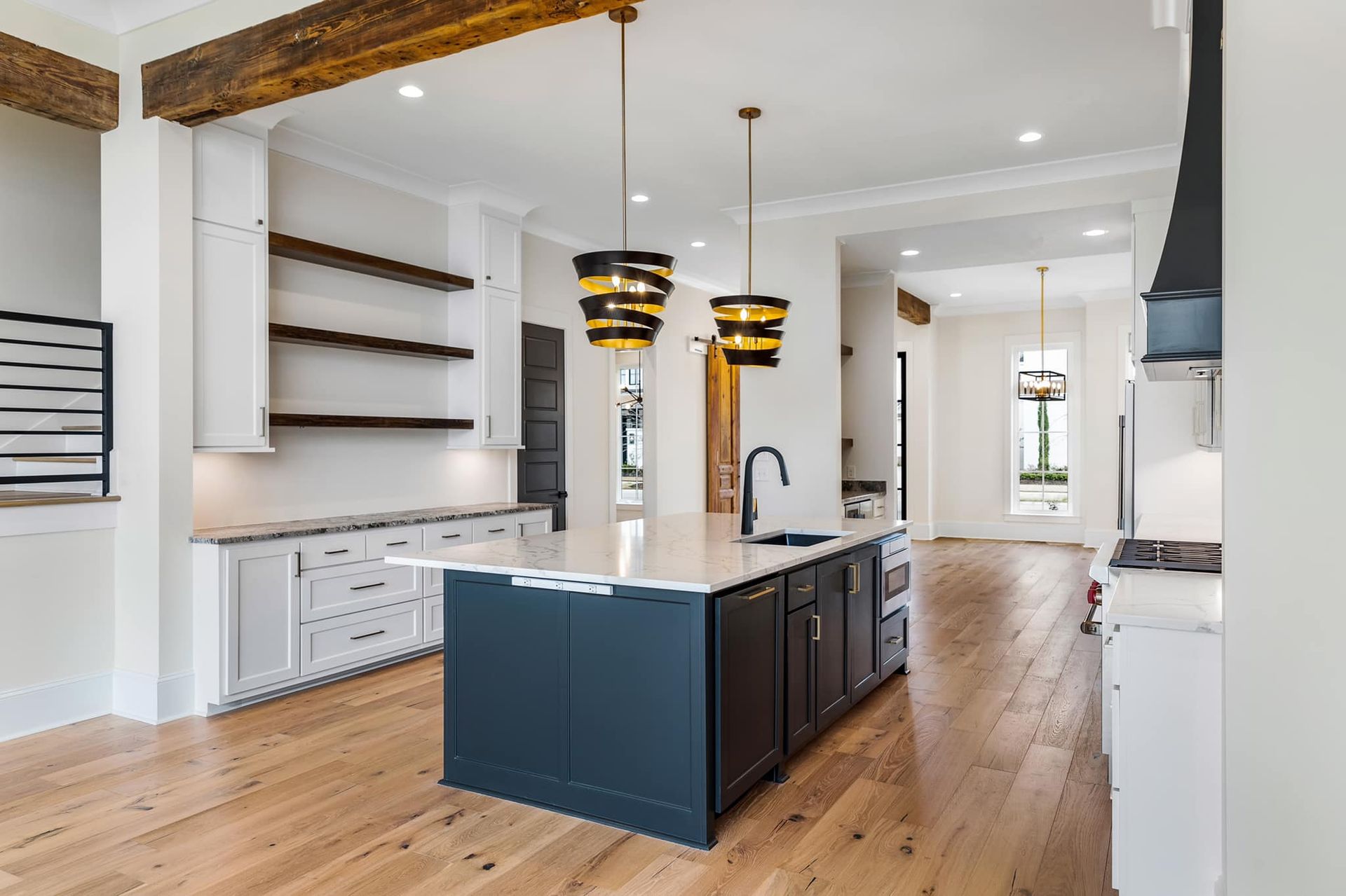 Modern kitchen with a dark blue island, light wood floors, and white cabinetry.
