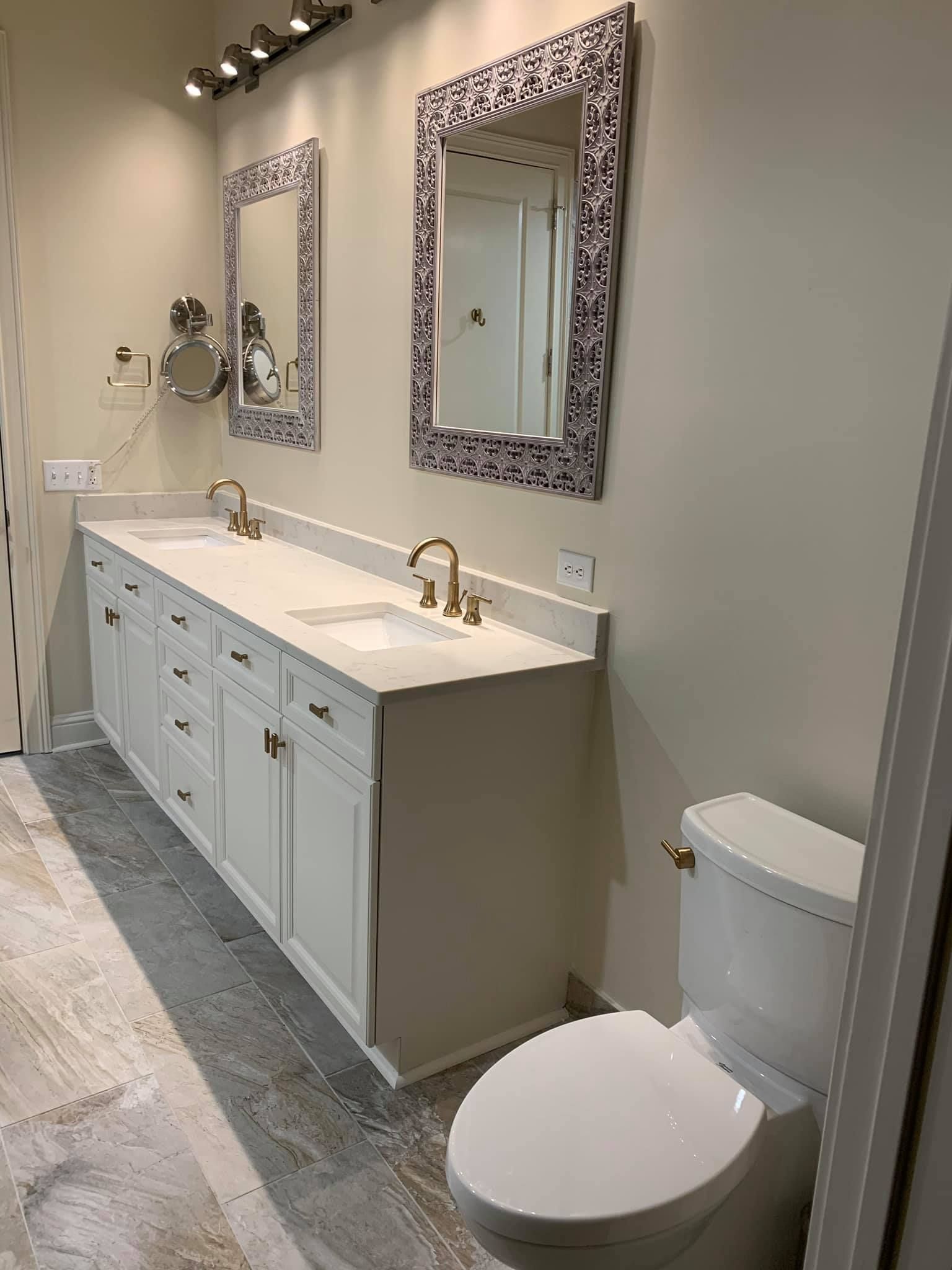 Bathroom with white vanity, sinks, mirrors, and toilet. Gray and white flooring, neutral walls.