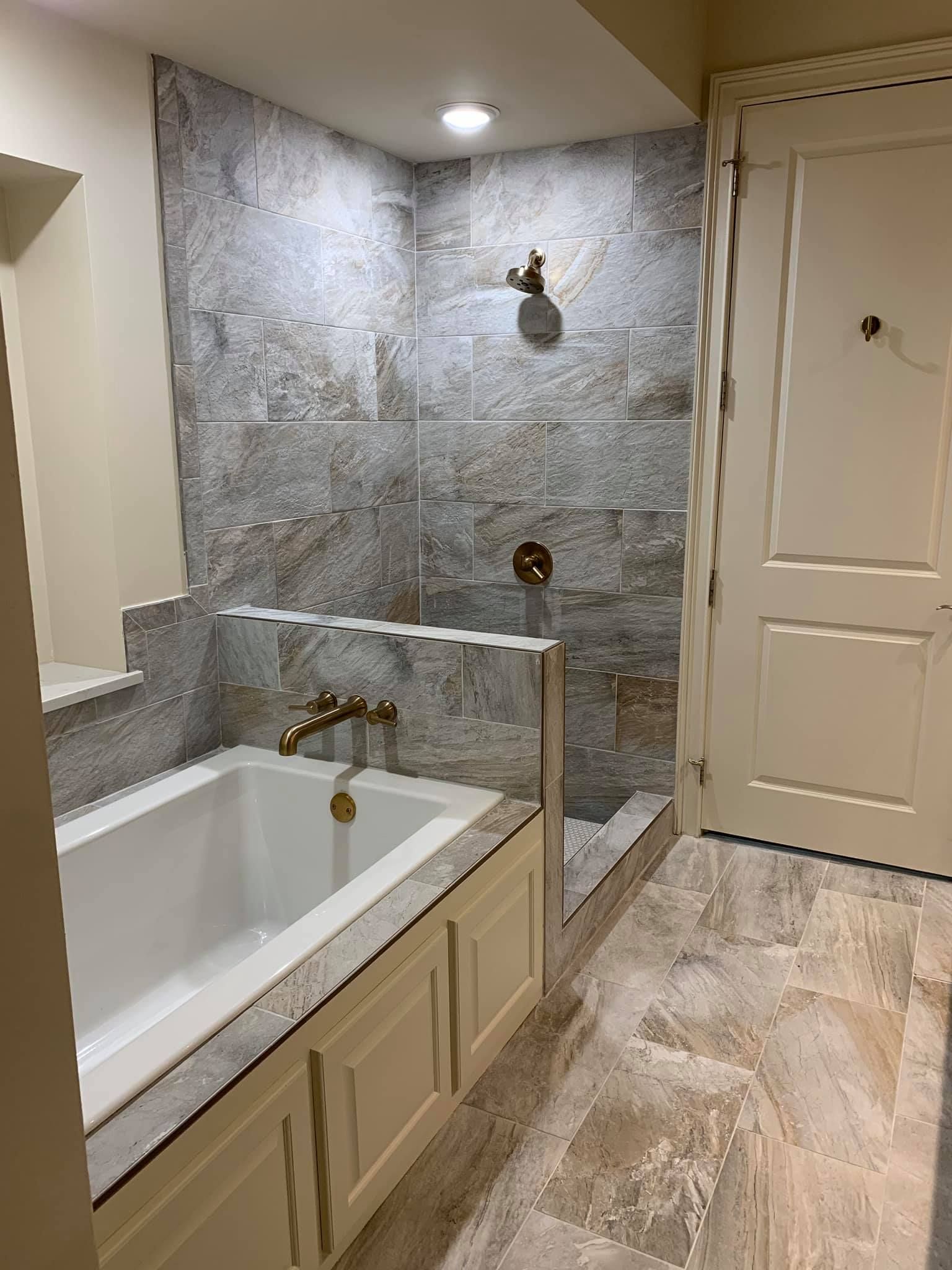Bathroom with a white bathtub, gold fixtures, and gray tile shower.